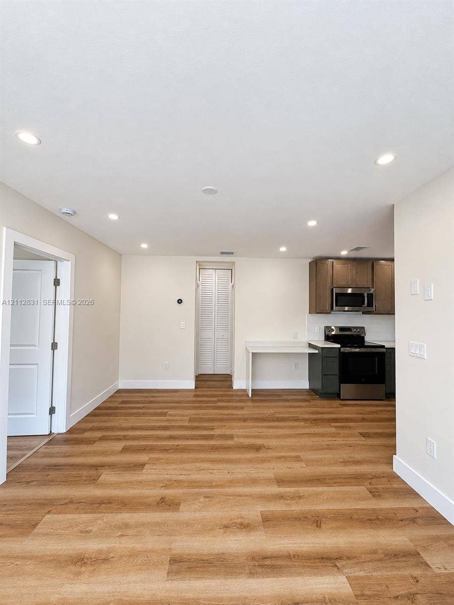 Open-concept interior featuring wood-finish flooring, recessed lighting, white cabinetry, integrated stainless steel appliances, and a built-in counter surface