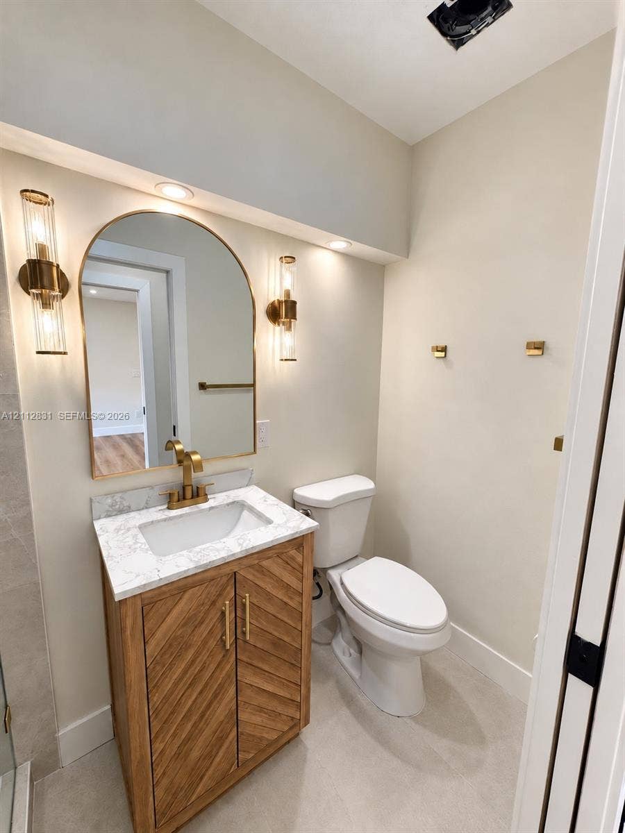 Vanity featuring a chevron-patterned wood cabinet, stone-finish countertop, arched mirror, brass-finish fixtures, and dual-sconce wall lighting