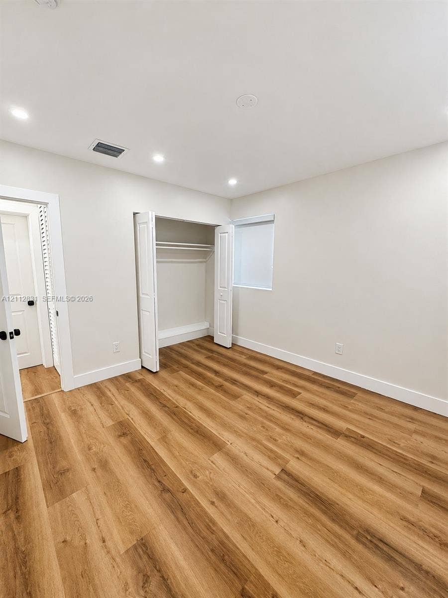 Interior room featuring wood-finish flooring, recessed lighting, neutral wall paint, and a built-in closet with double-hinged doors