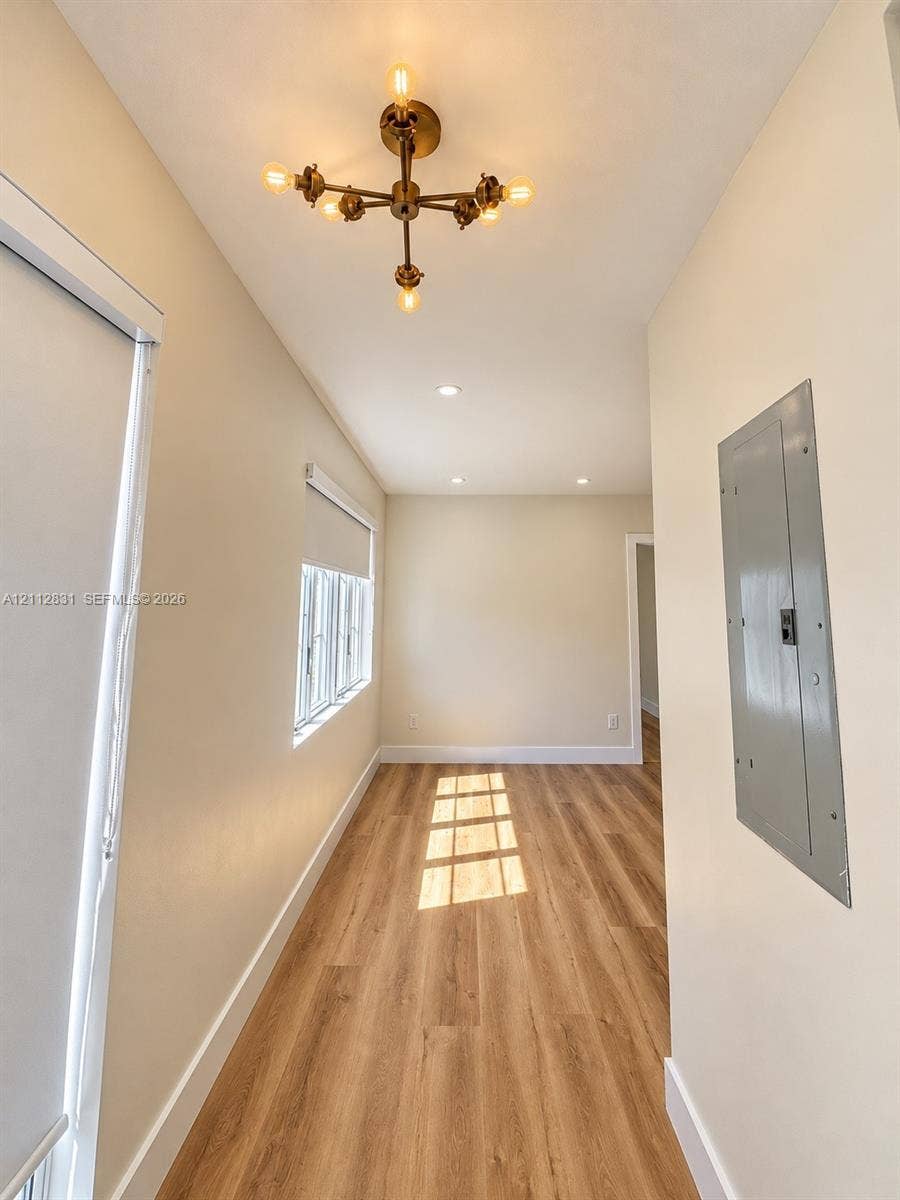 Wood-finish flooring, multi-light metallic chandelier, recessed ceiling lighting, and windows featuring roller shades