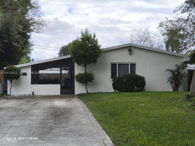 1411 N 65th Avenue, Hollywood, FL 33024 Painted brick exterior featuring a covered patio, concrete driveway, and attached metal wall-mounted lighting