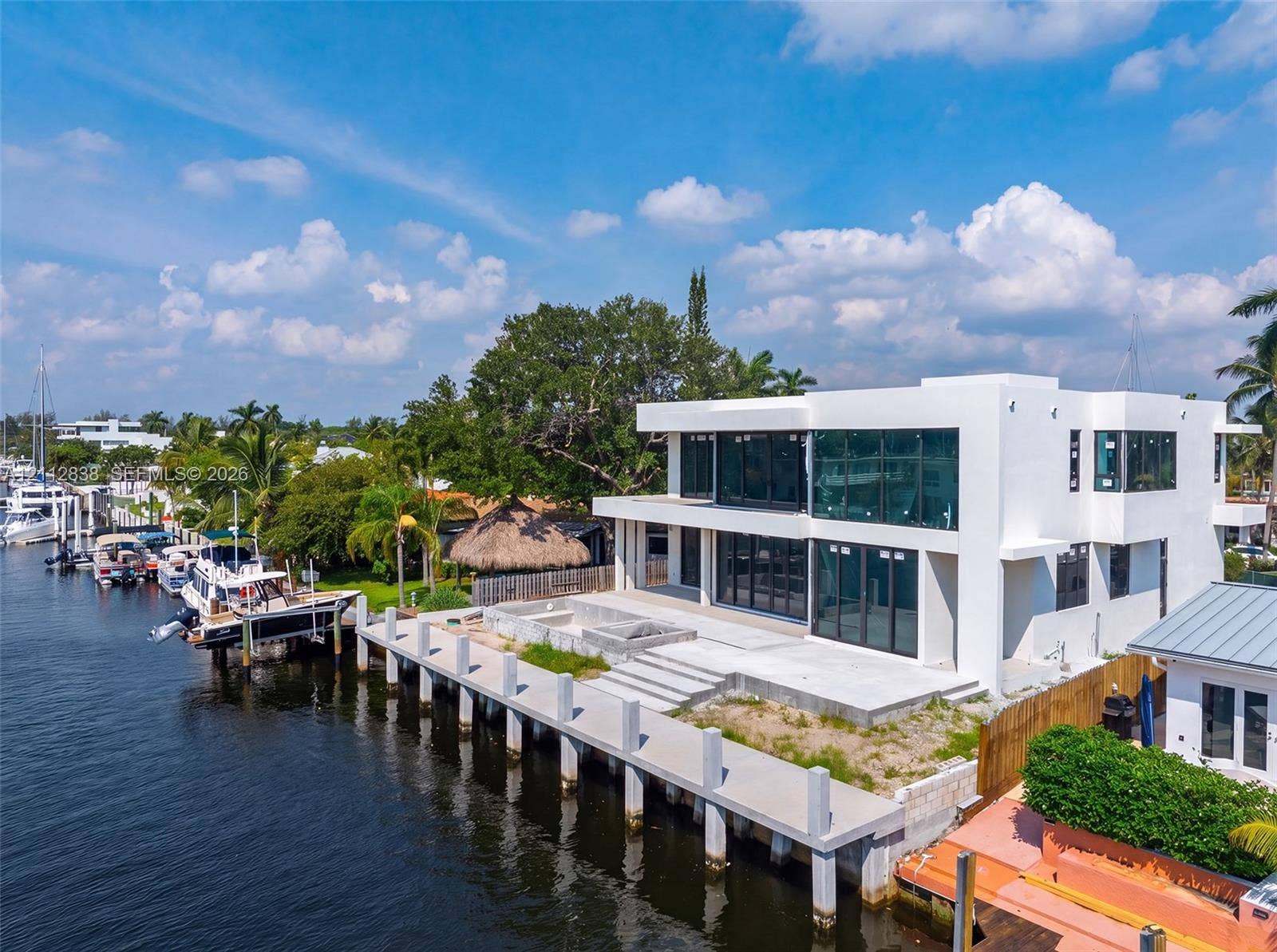 Contemporary waterfront residence featuring a concrete dock, expansive glass-paneled exterior, dual-level outdoor terrace, and a built-in fire feature