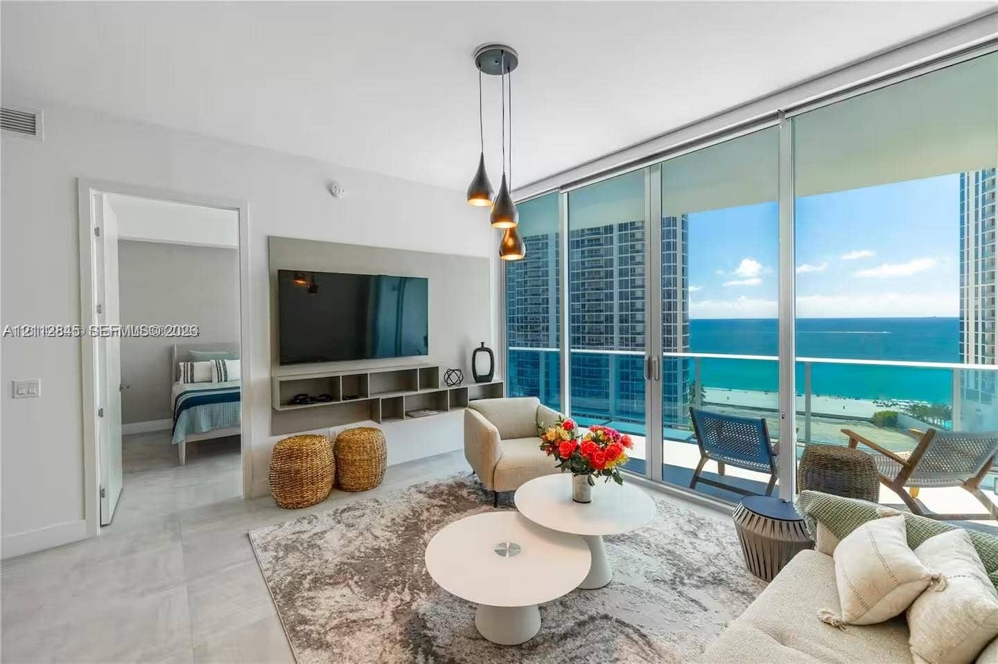 17550 Collins Avenue, #1202, Sunny Isles Beach, Sunny Isles Beach, FL 33160 Floor-to-ceiling glass wall with ocean backdrop, private balcony, neutral large-format tile flooring, built-in wall-mounted media console, and triple-pendant light fixture