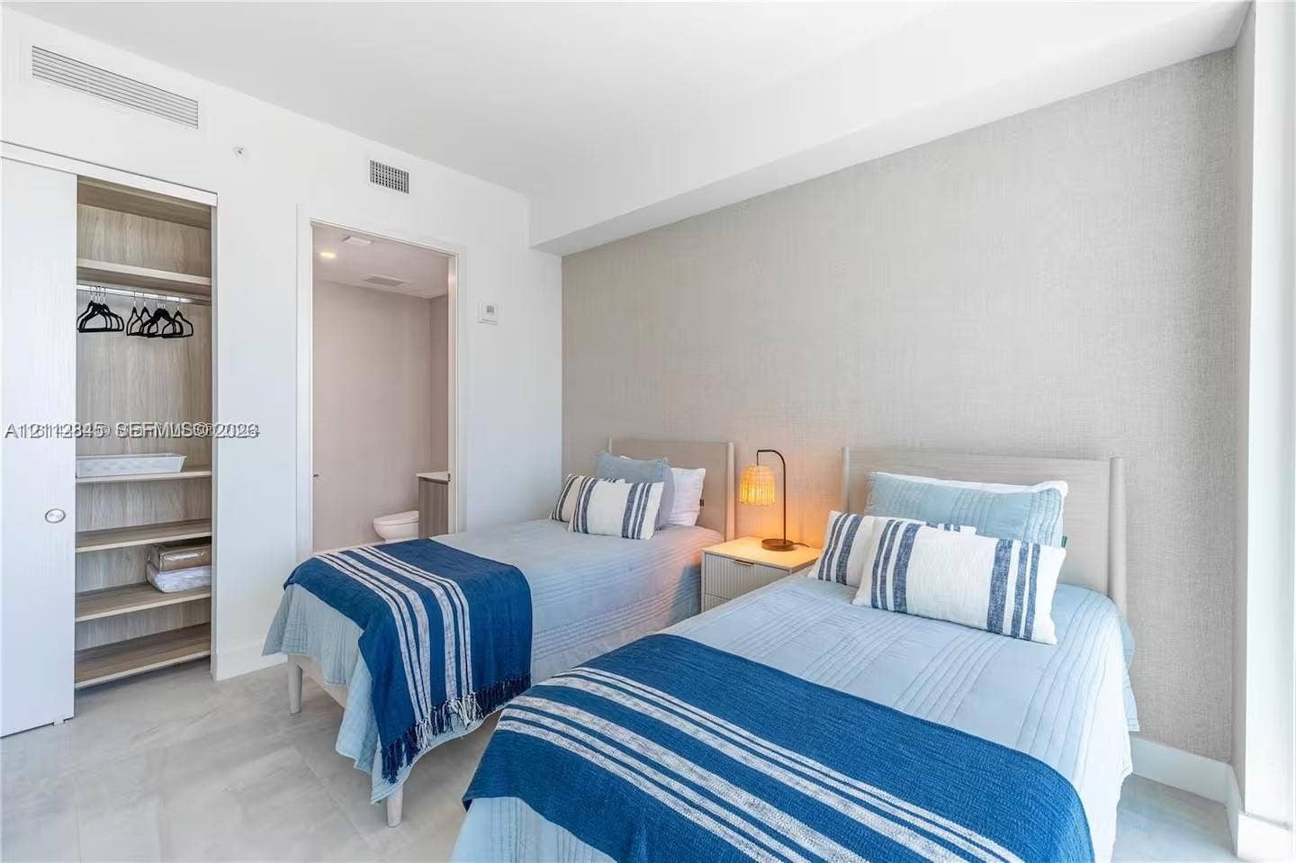 17550 Collins Avenue, #1202, Sunny Isles Beach, Sunny Isles Beach, FL 33160 Bedroom featuring neutral-toned textured wall covering, wood-finish shelving within an integrated closet, and light-toned flooring