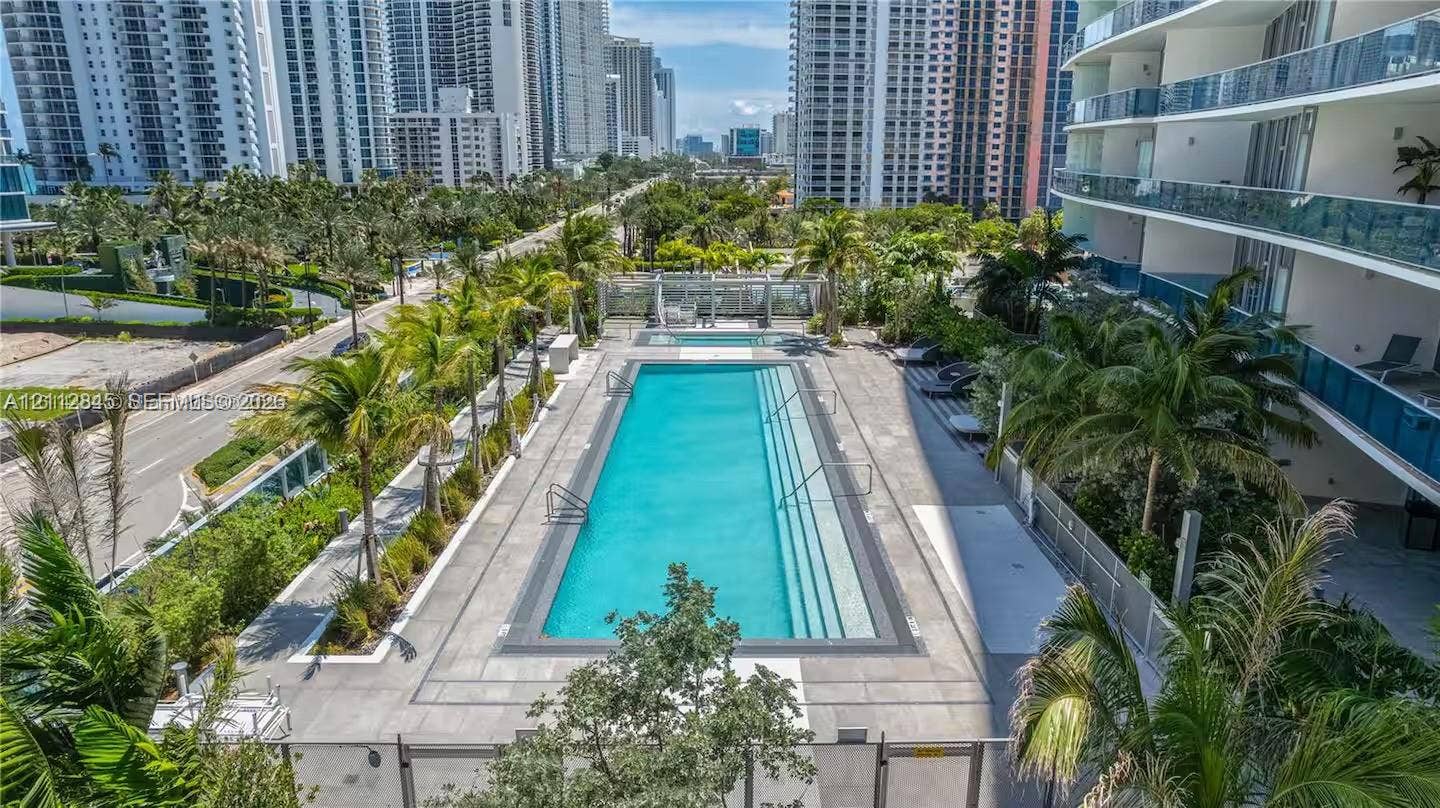 17550 Collins Avenue, #1202, Sunny Isles Beach, Sunny Isles Beach, FL 33160 Rectangular swimming pool featuring integrated entry steps and stone paver decking surrounded by mature palm trees and glass-railed balconies