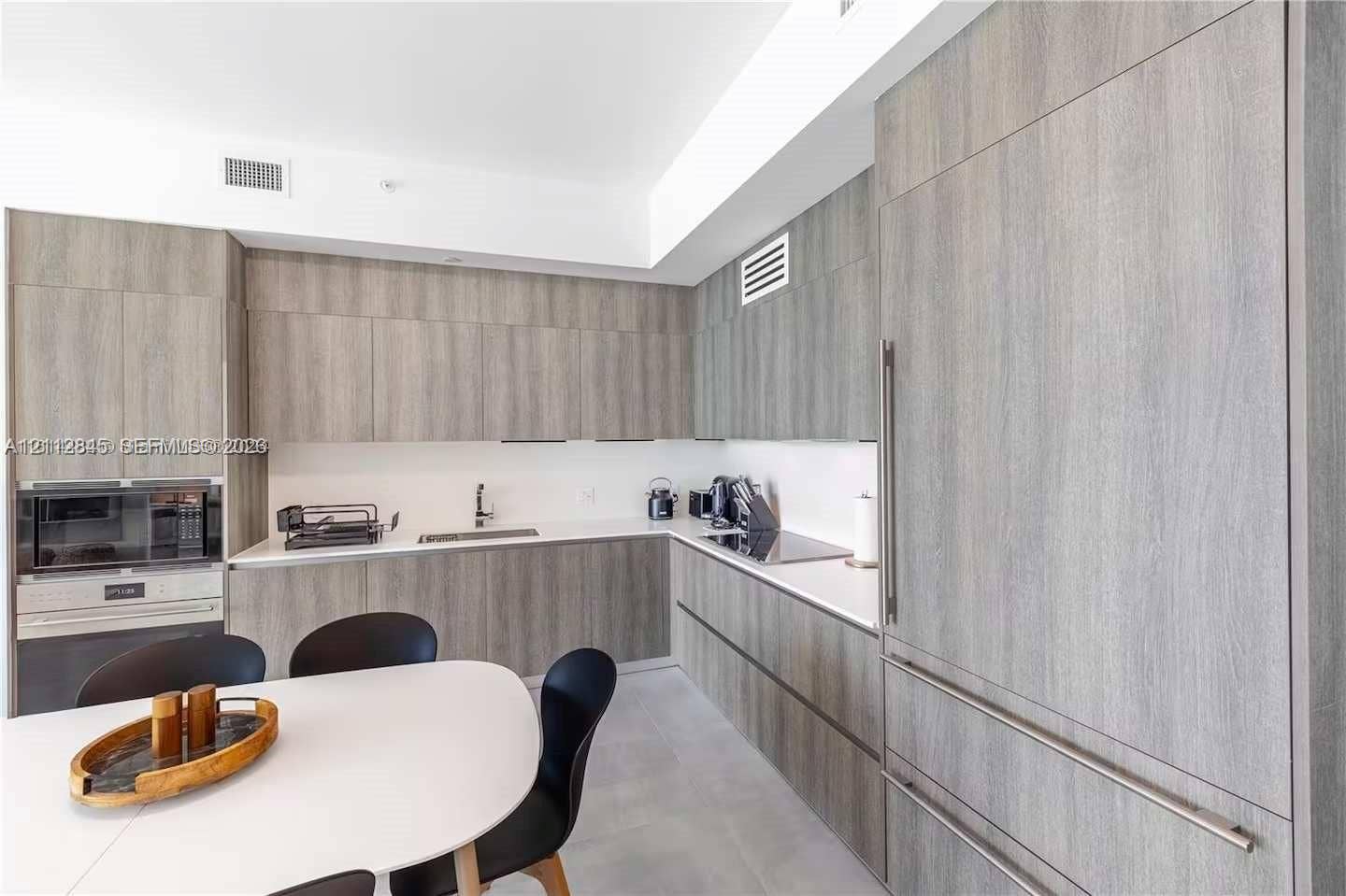 17550 Collins Avenue, #1202, Sunny Isles Beach, Sunny Isles Beach, FL 33160 Kitchen featuring flat-panel wood-finish cabinetry, integrated panel-ready refrigerator, solid-surface countertops, built-in microwave, and flush-mount cooktop