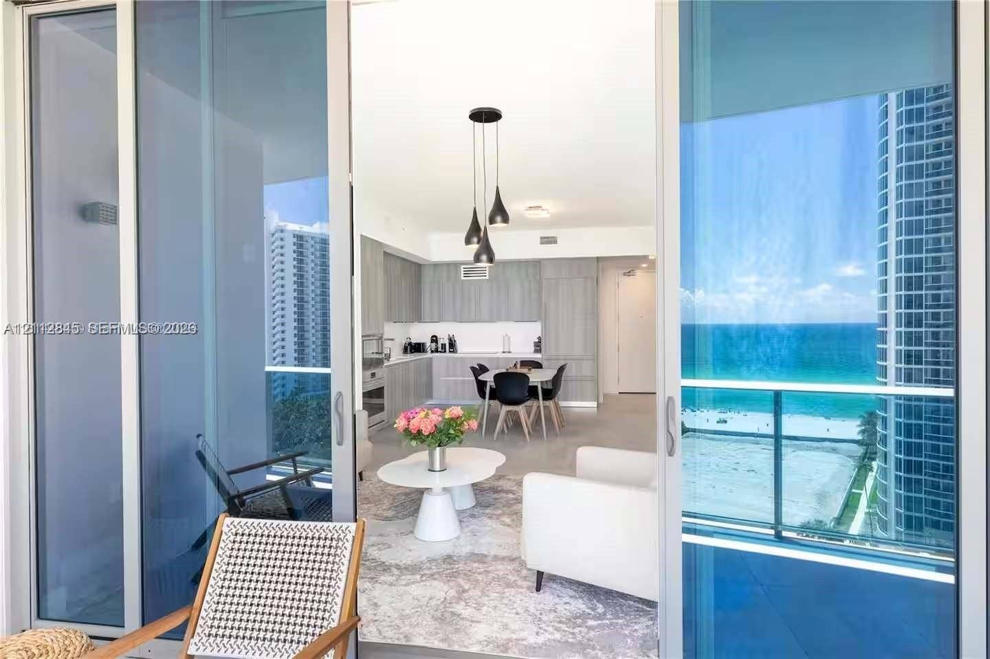 17550 Collins Avenue, #1202, Sunny Isles Beach, Sunny Isles Beach, FL 33160 Full-height sliding glass doors opening to a covered balcony, integrated kitchen cabinetry, recessed ceiling lighting, pendant light fixture, and ocean scenery