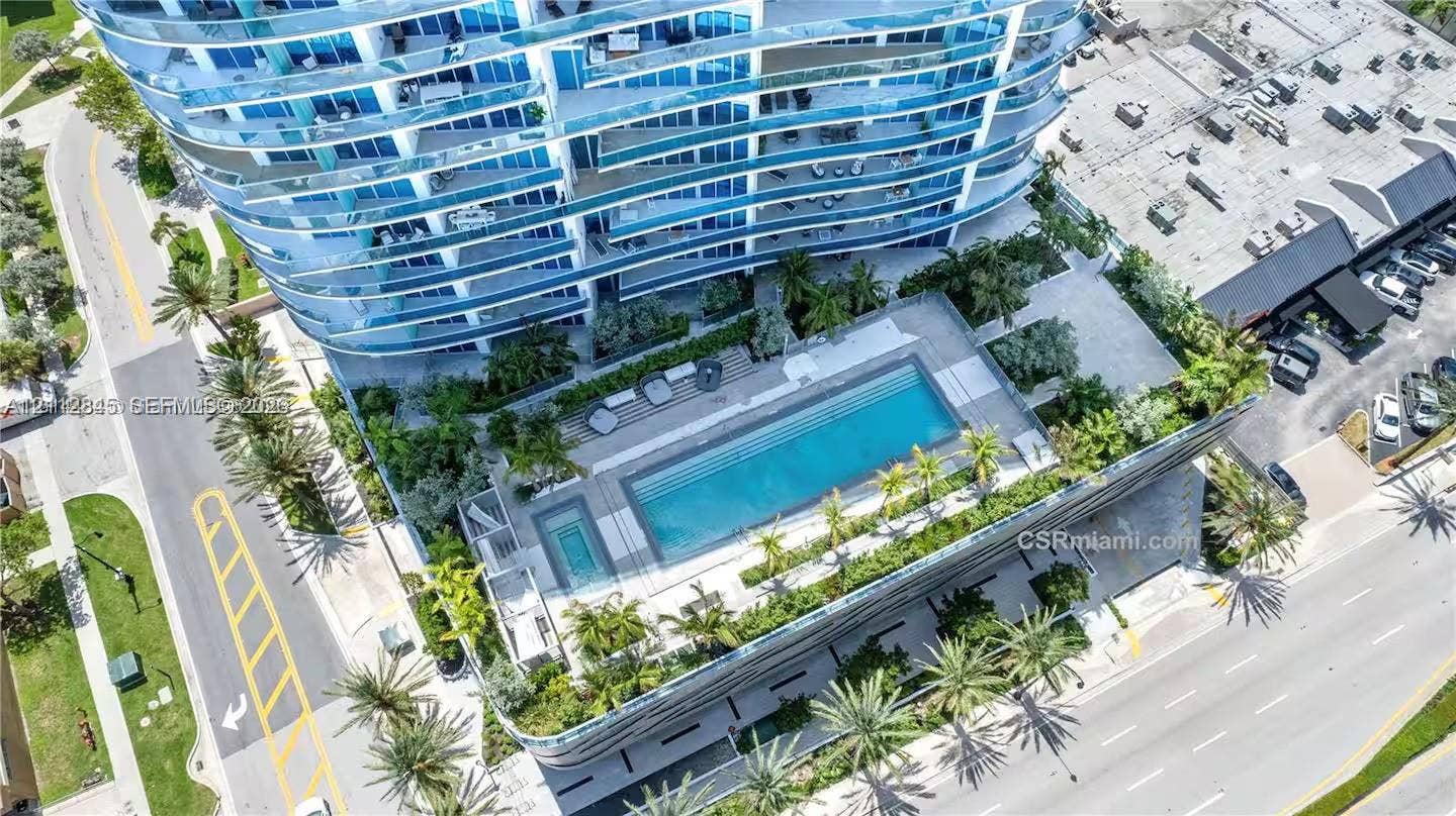 17550 Collins Avenue, #1202, Sunny Isles Beach, Sunny Isles Beach, FL 33160 High-rise building featuring curvilinear architecture with glass balcony railings, an expansive ground-level swimming pool, a dedicated spa, and integrated tropical landscaping