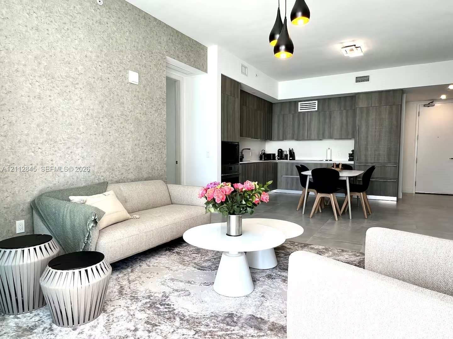 17550 Collins Avenue, #1202, Sunny Isles Beach, Sunny Isles Beach, FL 33160 Open-concept living space featuring textured accent wallpaper, flat-panel dark wood-finish cabinetry, built-in stainless steel appliances, large-format tile flooring, and multi-pendant contemporary lighting
