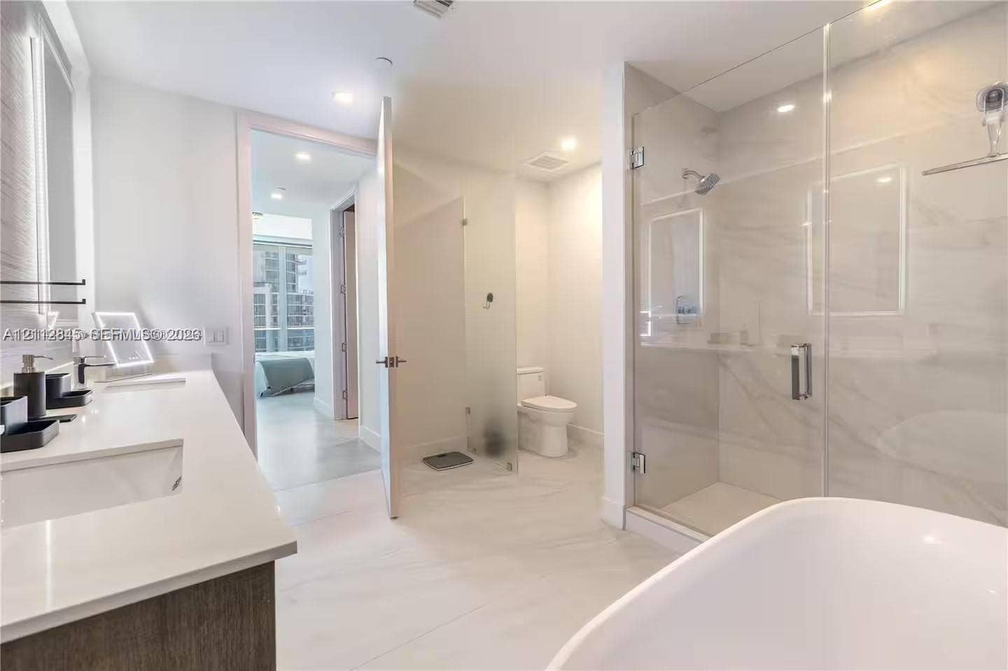 17550 Collins Avenue, #1202, Sunny Isles Beach, Sunny Isles Beach, FL 33160 Bathroom featuring a dual-sink vanity with light-colored countertops, a freestanding soaking tub, and a glass-enclosed shower with tiled surround