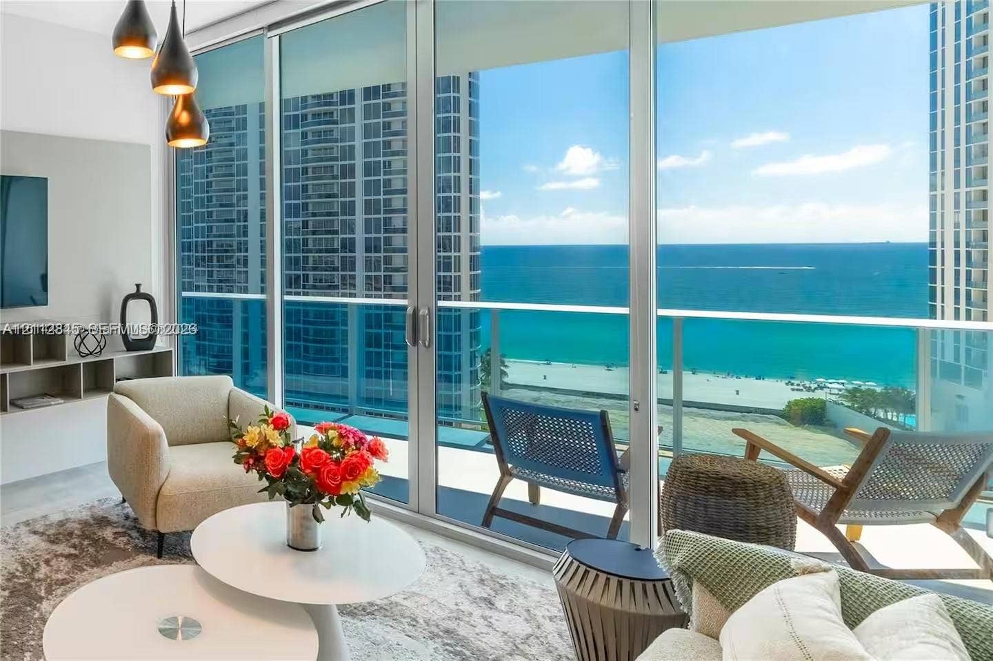17550 Collins Avenue, #1202, Sunny Isles Beach, Sunny Isles Beach, FL 33160 Floor-to-ceiling glass walls, expansive balcony with glass railings, built-in media shelving, and trio of pendant light fixtures