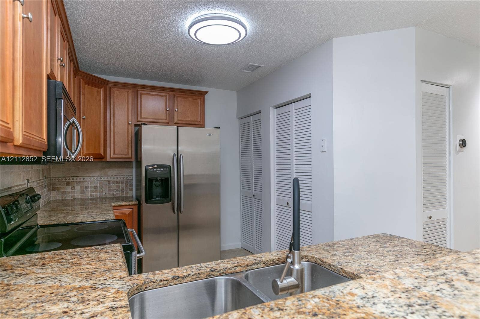 5741 Riverside Drive, #205A5, Coral Springs, Coral Springs, FL 33067 Kitchen featuring stone-patterned countertops, wood cabinetry, stainless steel appliances, dual-basin stainless steel sink with high-arc faucet, and tiled backsplash