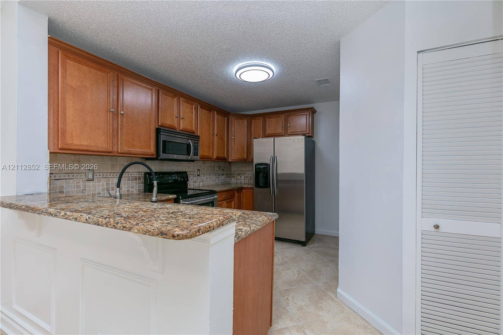 5741 Riverside Drive, #205A5, Coral Springs, Coral Springs, FL 33067 Kitchen featuring natural wood cabinetry, stone-finish countertops, stainless steel appliances, a decorative tiled backsplash, and tile flooring