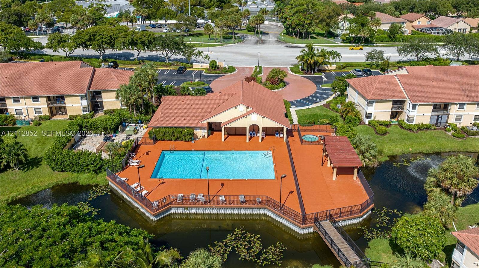 5741 Riverside Drive, #205A5, Coral Springs, Coral Springs, FL 33067 Community pool area featuring a perimeter deck, attached spa, covered pavilion, and pedestrian bridge over a water feature