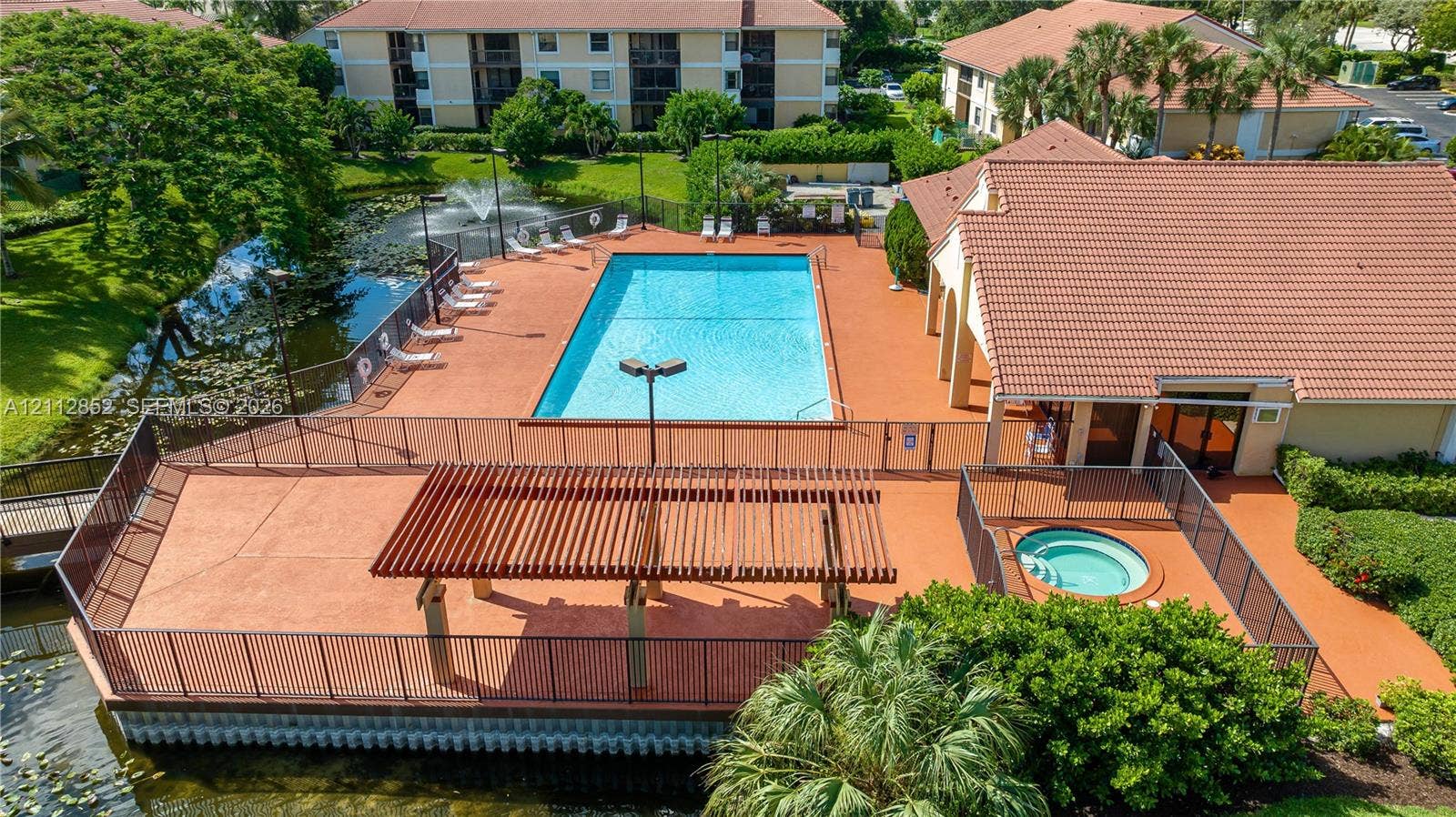 5741 Riverside Drive, #205A5, Coral Springs, Coral Springs, FL 33067 Community recreation area featuring a swimming pool, spa, water fountain, and wooden pergola set against a water feature