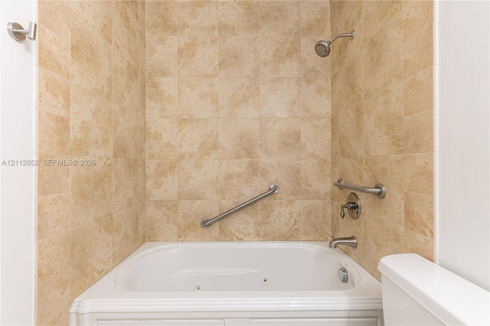 5741 Riverside Drive, #205A5, Coral Springs, Coral Springs, FL 33067 Jetted tub featuring stone-finish wall tiling, stainless steel wall-mounted grab bars, and a chrome shower fixture