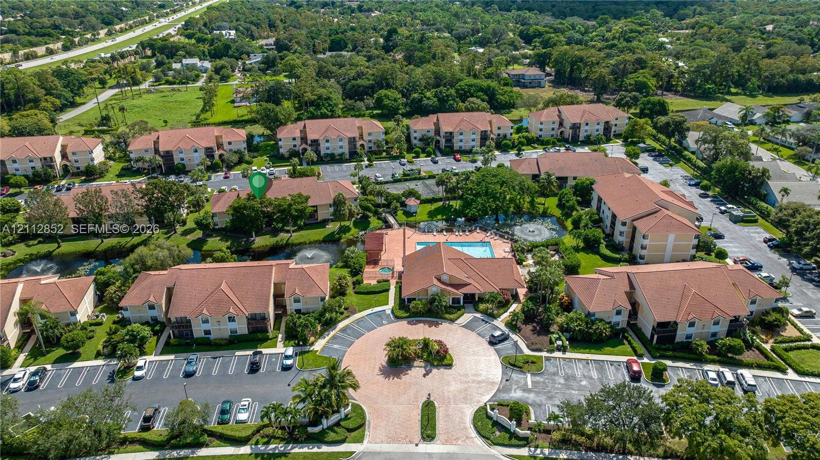 5741 Riverside Drive, #205A5, Coral Springs, Coral Springs, FL 33067 Aerial perspective of a multi-building residential complex featuring a central community swimming pool, paved roundabout entrance, designated parking areas, and landscaped grounds with water features