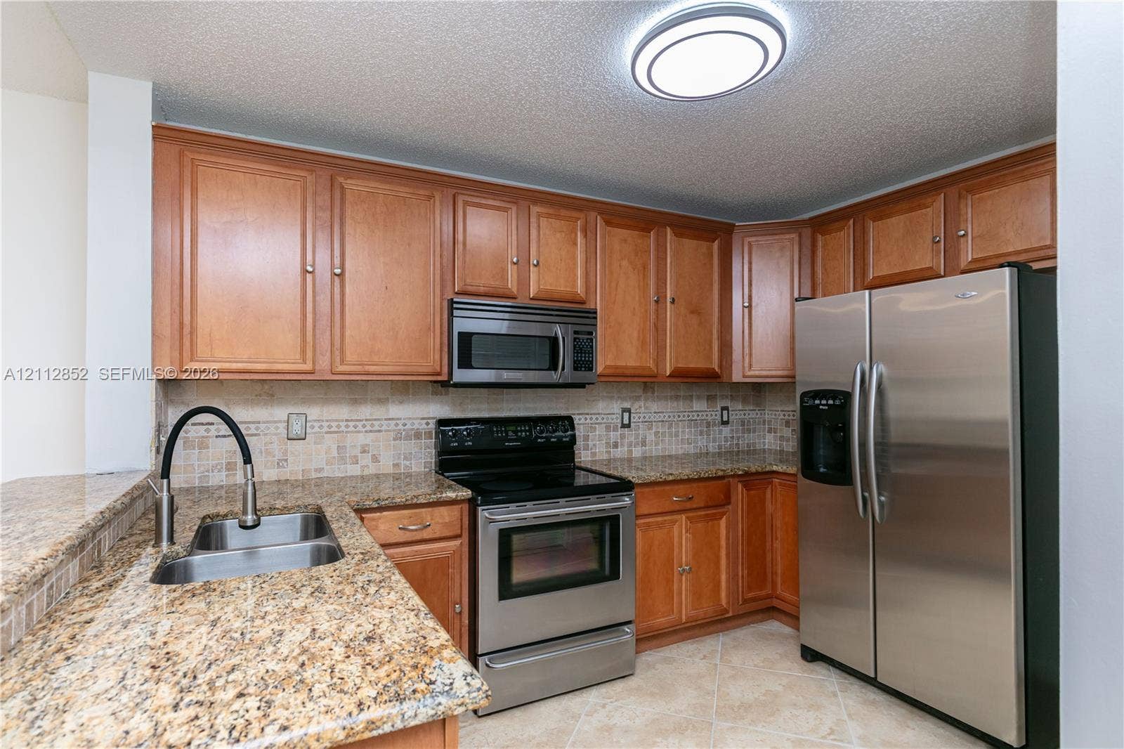 5741 Riverside Drive, #205A5, Coral Springs, Coral Springs, FL 33067 Kitchen featuring medium-tone wood cabinetry, stone countertops, stainless steel appliances, a tile backsplash, and a dual-basin undermount sink with a high-arch faucet