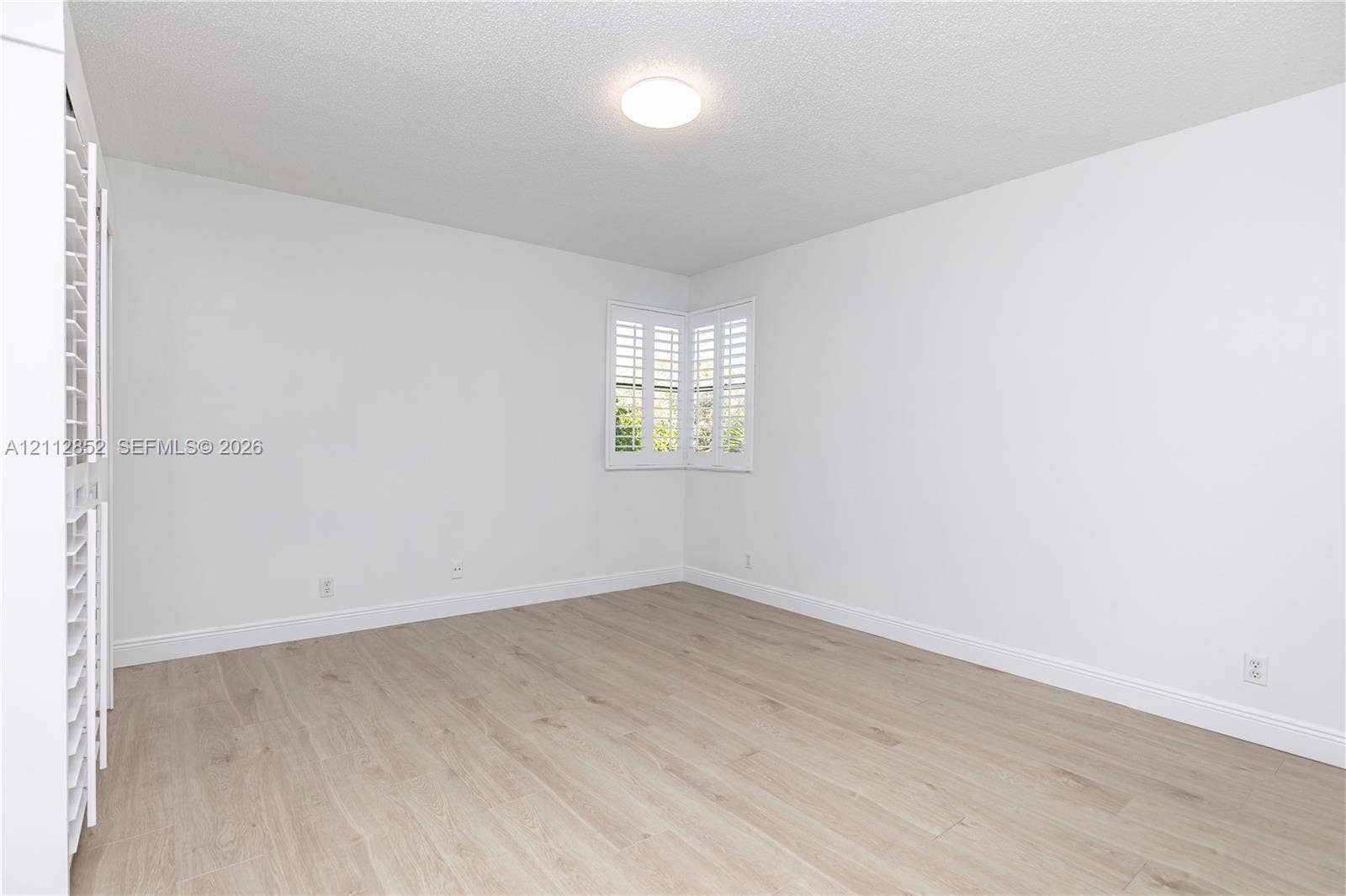 5741 Riverside Drive, #205A5, Coral Springs, Coral Springs, FL 33067 Neutral-toned room featuring wood-finish flooring, white plantation shutters, and a flush-mount ceiling light fixture