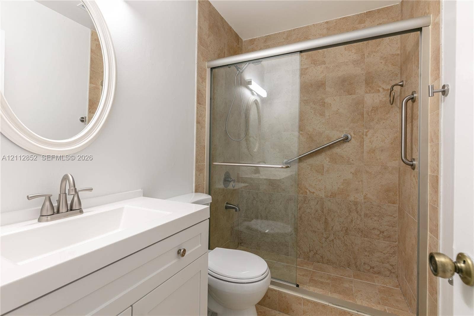 5741 Riverside Drive, #205A5, Coral Springs, Coral Springs, FL 33067 White vanity with integrated rectangular sink, oval wall-mounted mirror, and glass-enclosed shower with tiled surround and metal grab bars
