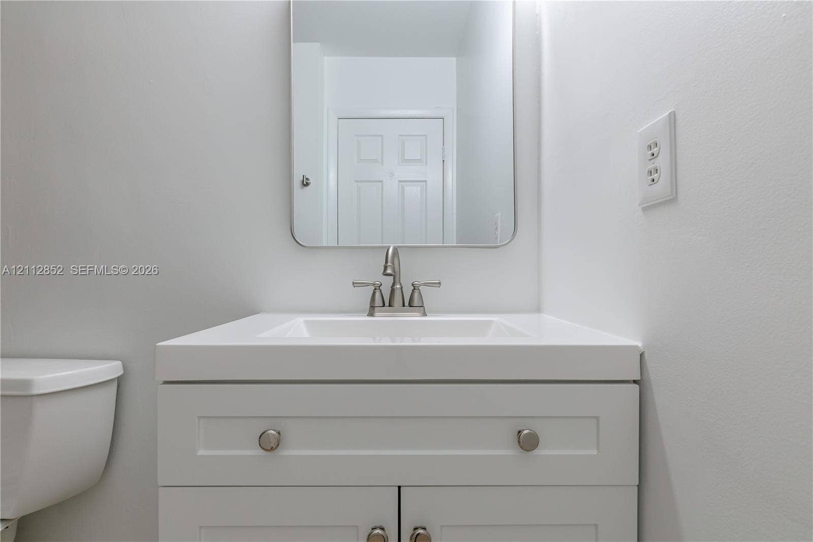 5741 Riverside Drive, #205A5, Coral Springs, Coral Springs, FL 33067 White vanity cabinet featuring a solid surface countertop with integrated basin, polished metal double-handle faucet, and rounded rectangular mirror