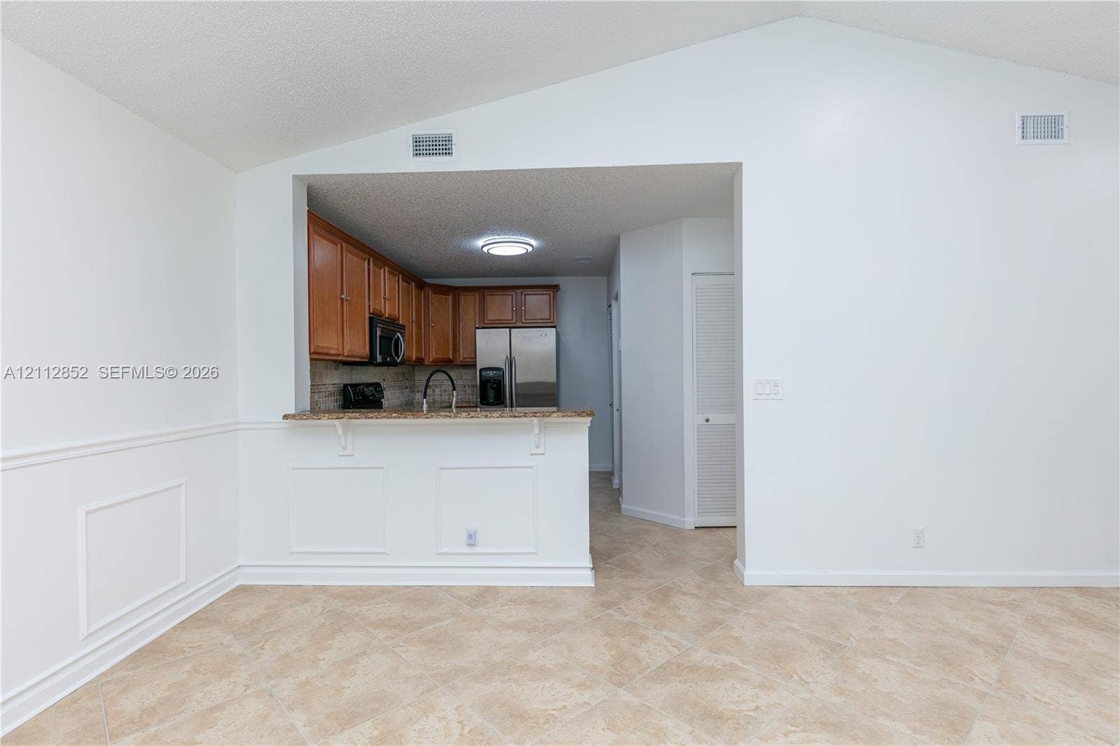 5741 Riverside Drive, #205A5, Coral Springs, Coral Springs, FL 33067 Vaulted ceiling featuring a breakfast bar with stone-finish countertop, wooden cabinetry, stone backsplash, and neutral tile flooring