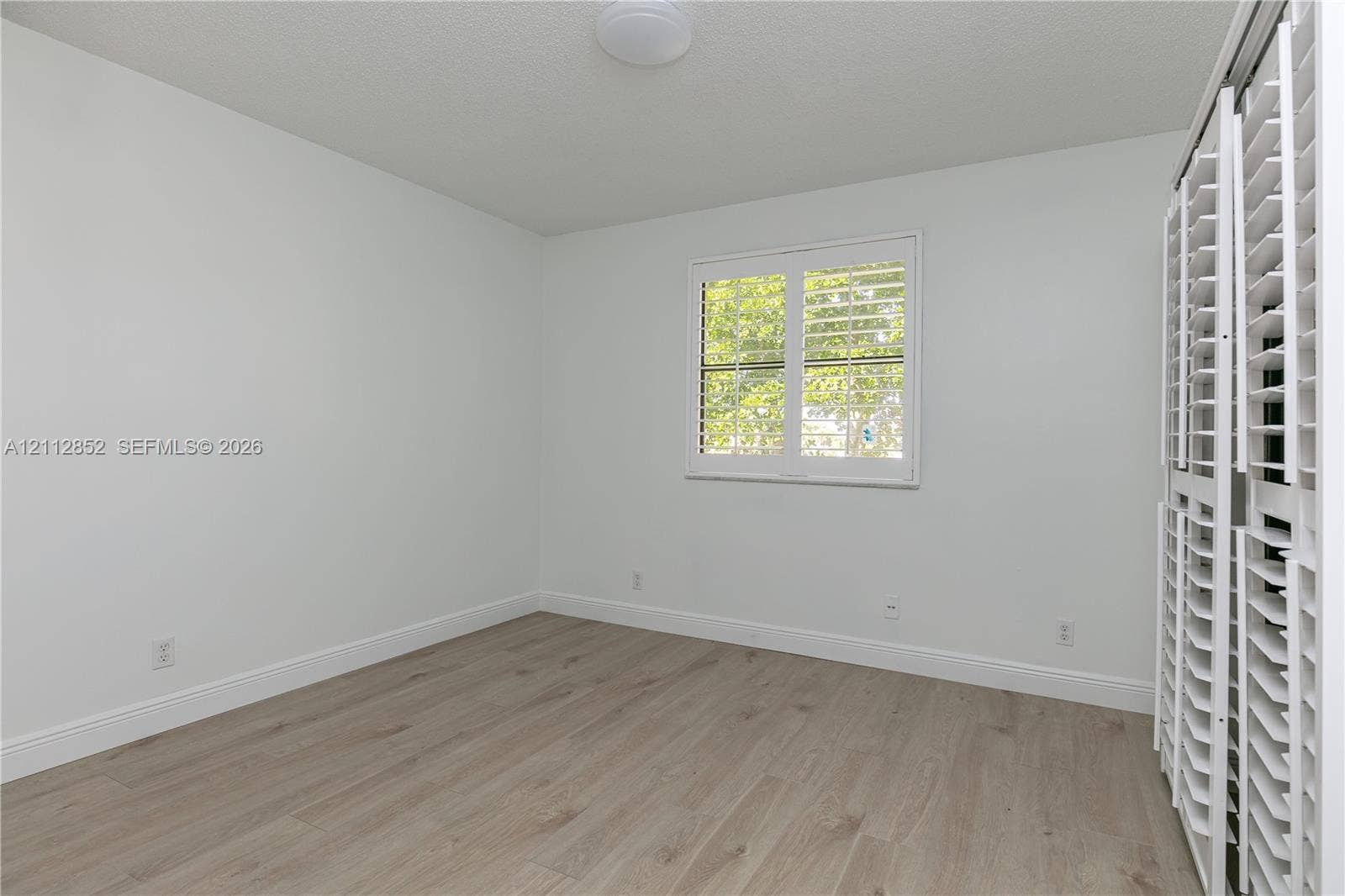 5741 Riverside Drive, #205A5, Coral Springs, Coral Springs, FL 33067 Room featuring wood-finish flooring, a window with louvered shutters, and bi-fold louvered closet doors