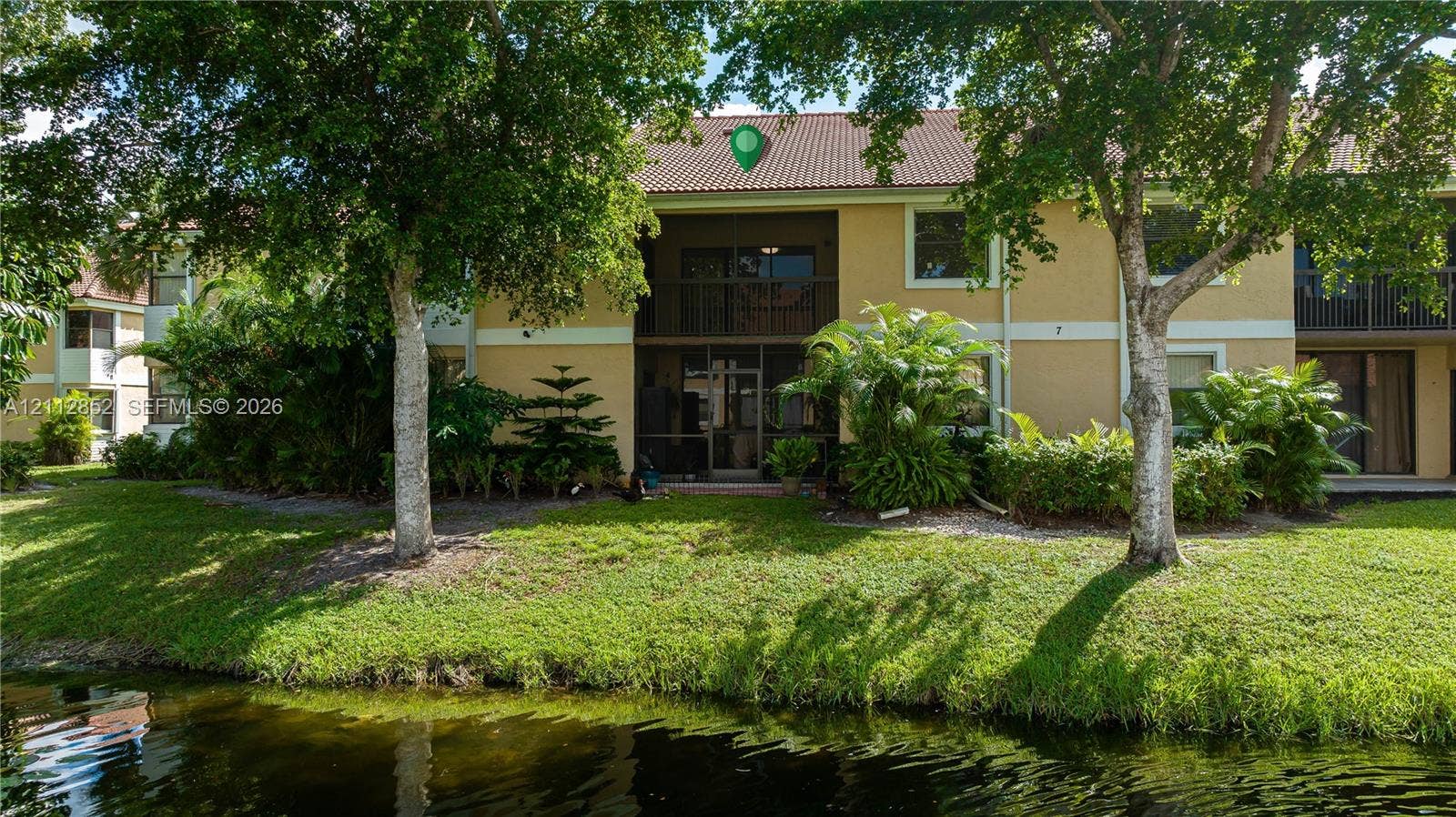 5741 Riverside Drive, #205A5, Coral Springs, Coral Springs, FL 33067 Two-story exterior featuring a tile roof, stucco finish, screened balcony, and water frontage with mature landscaping