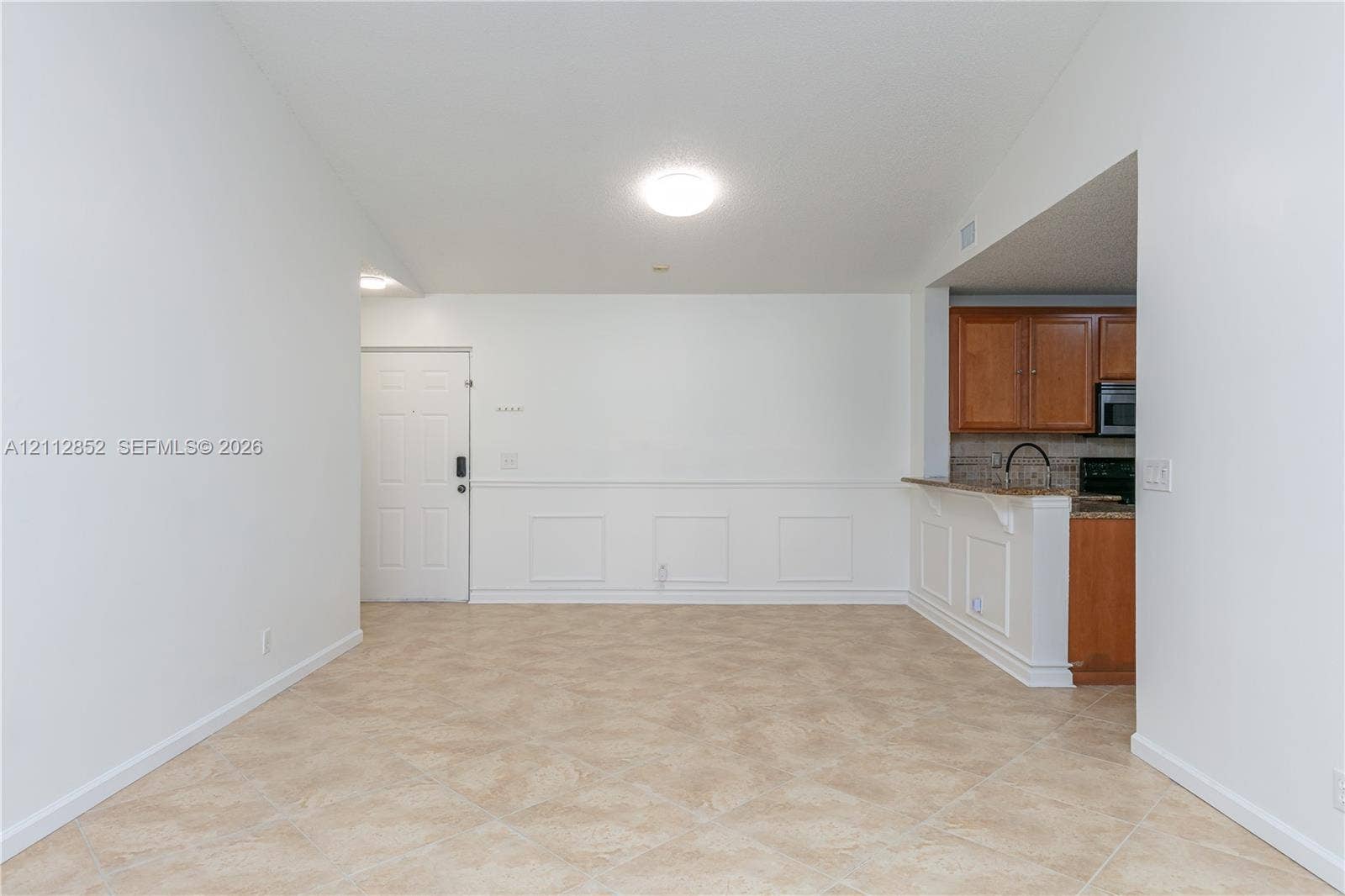 5741 Riverside Drive, #205A5, Coral Springs, Coral Springs, FL 33067 Interior space featuring ceramic tile flooring, wainscoting detail, vaulted ceiling, flush-mount lighting, and kitchen cabinetry with a breakfast bar