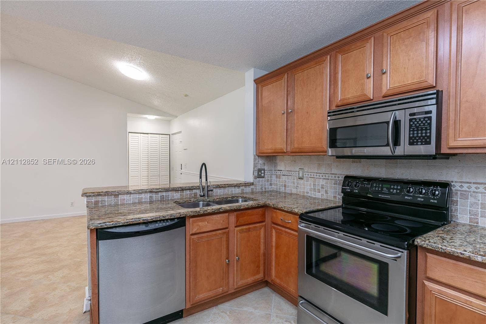 5741 Riverside Drive, #205A5, Coral Springs, Coral Springs, FL 33067 Kitchen featuring natural wood cabinetry, stone-surface countertops, stone tile backsplash, stainless steel appliances, and a double-basin sink with a high-arch pull-down faucet