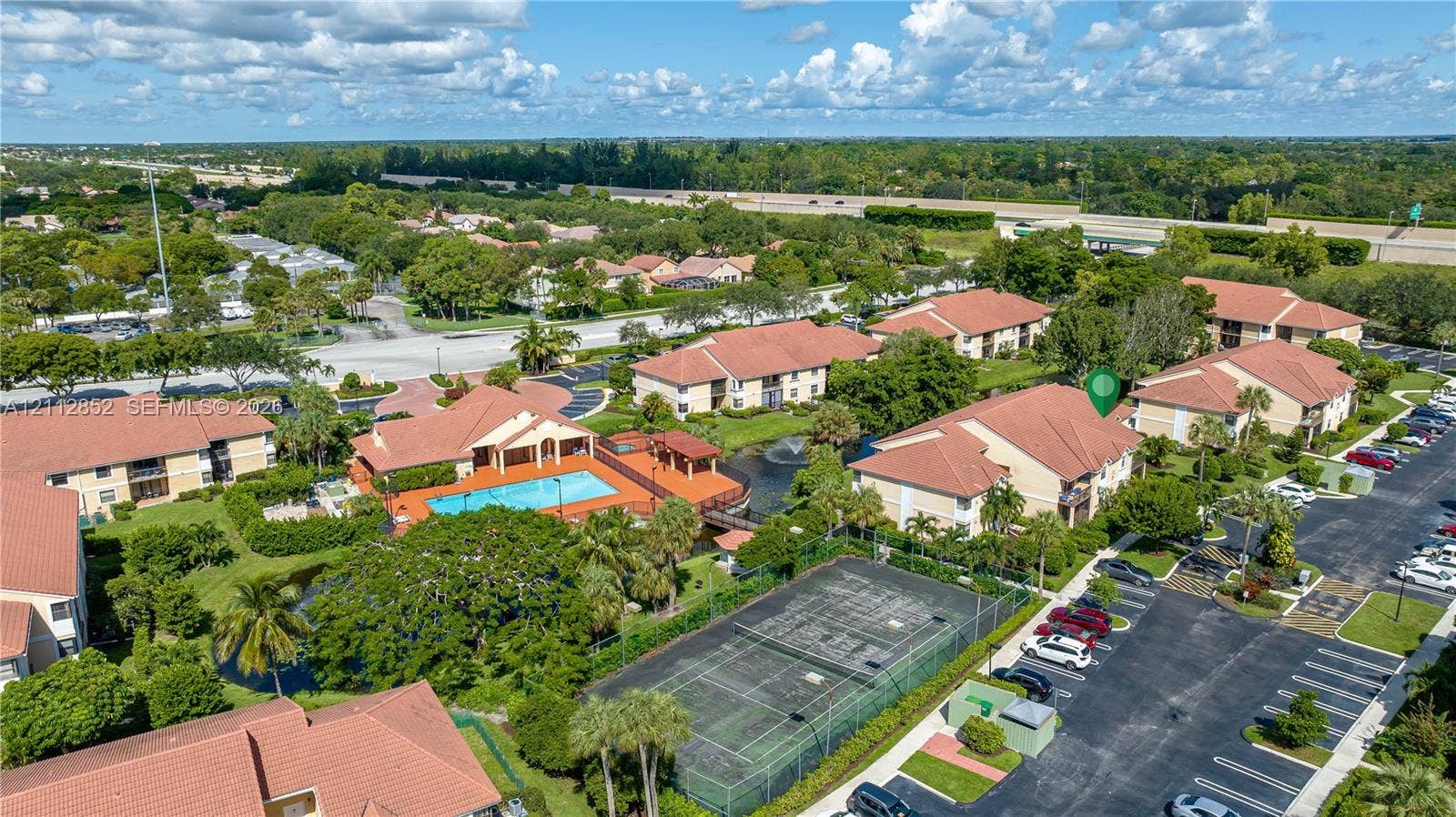 5741 Riverside Drive, #205A5, Coral Springs, Coral Springs, FL 33067 Aerial view of a residential community featuring a multi-story building, an outdoor swimming pool, a tennis court, and paved parking areas amidst landscaped grounds