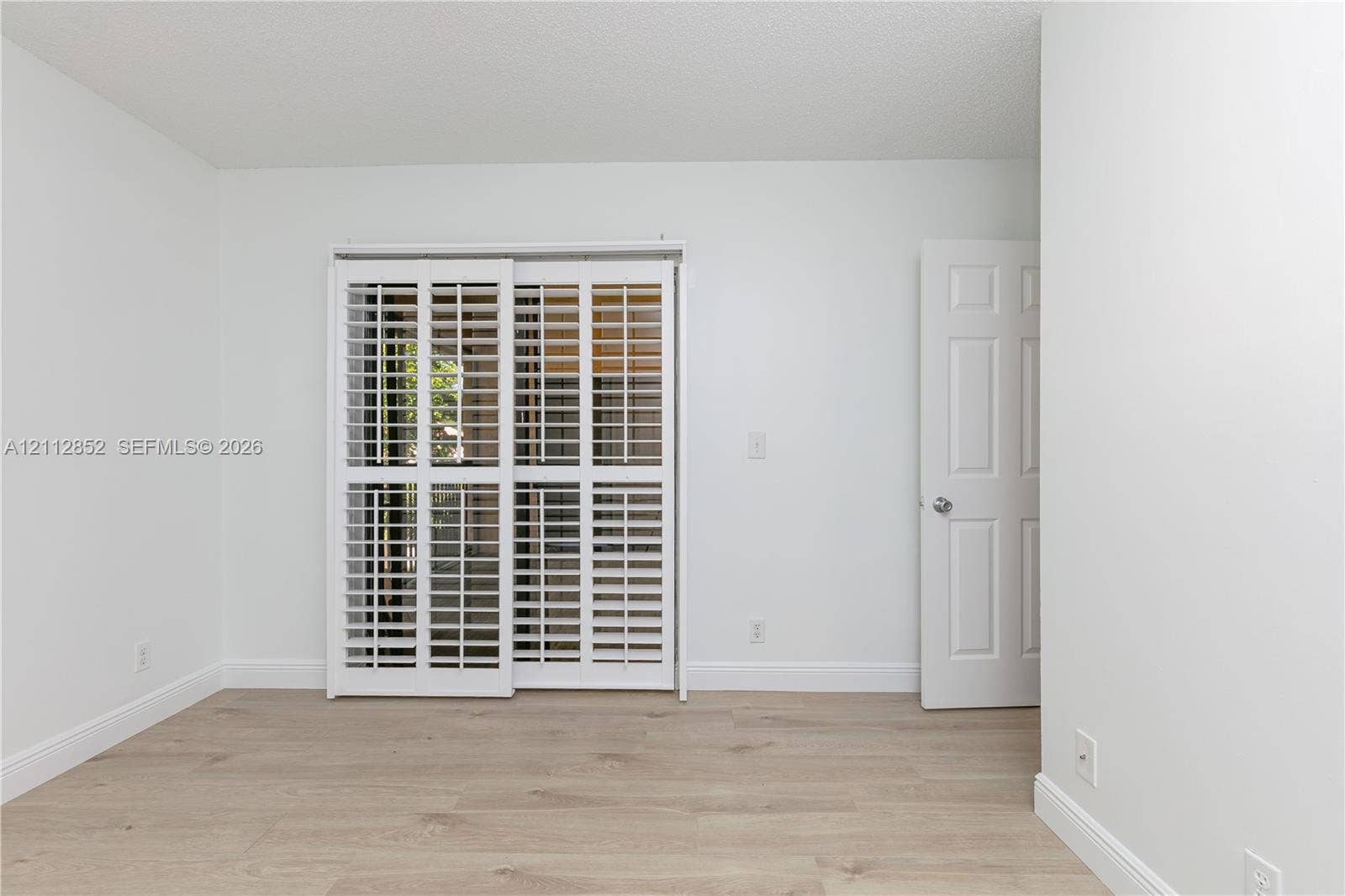 5741 Riverside Drive, #205A5, Coral Springs, Coral Springs, FL 33067 Interior space featuring light-toned wood-finish flooring, white walls, white plantation shutters on sliding doors, and a paneled swing door