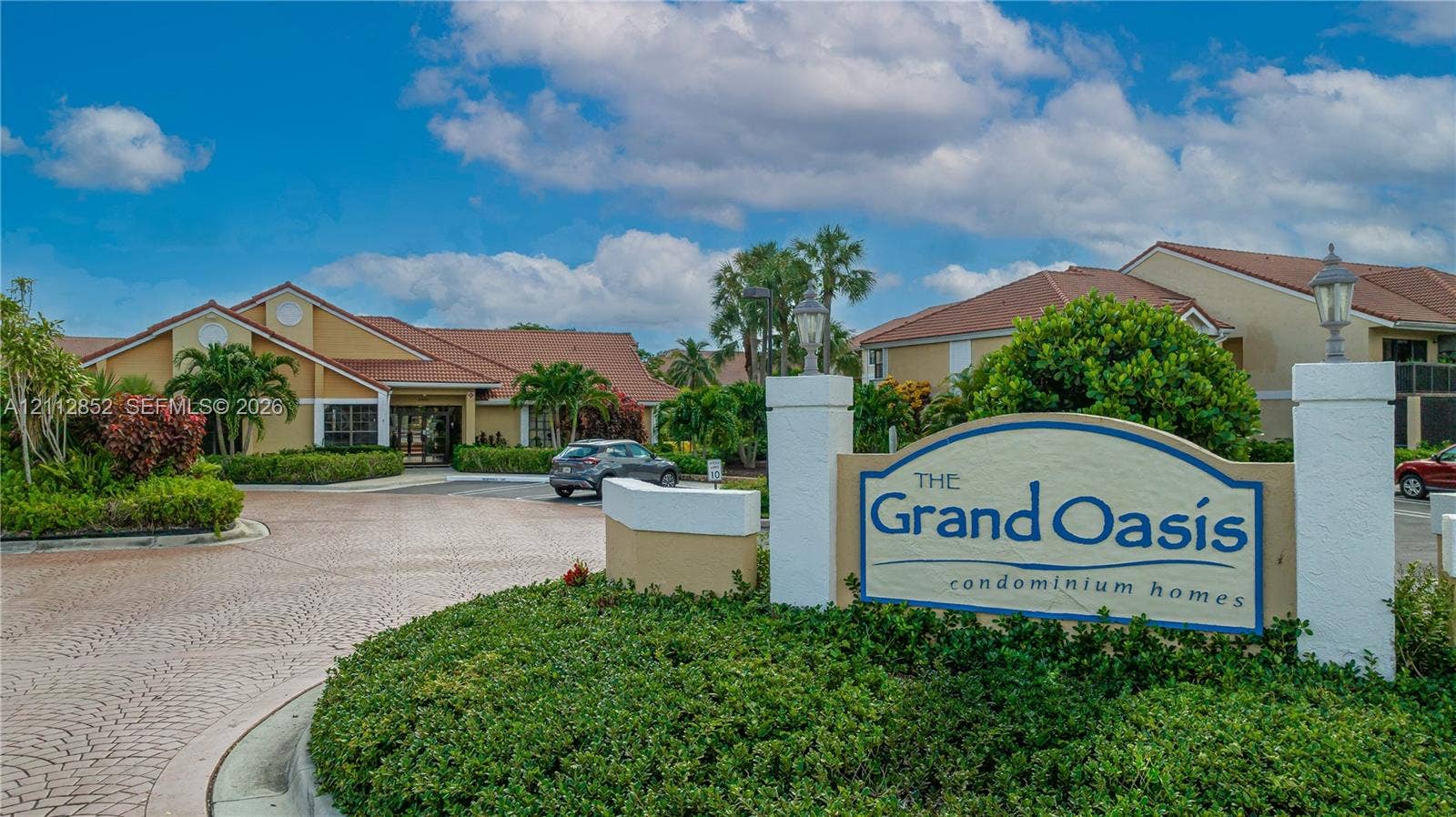 5741 Riverside Drive, #205A5, Coral Springs, Coral Springs, FL 33067 Community entrance featuring decorative stamped concrete paving, mature tropical landscaping, and a masonry monument sign with integrated pillar lighting