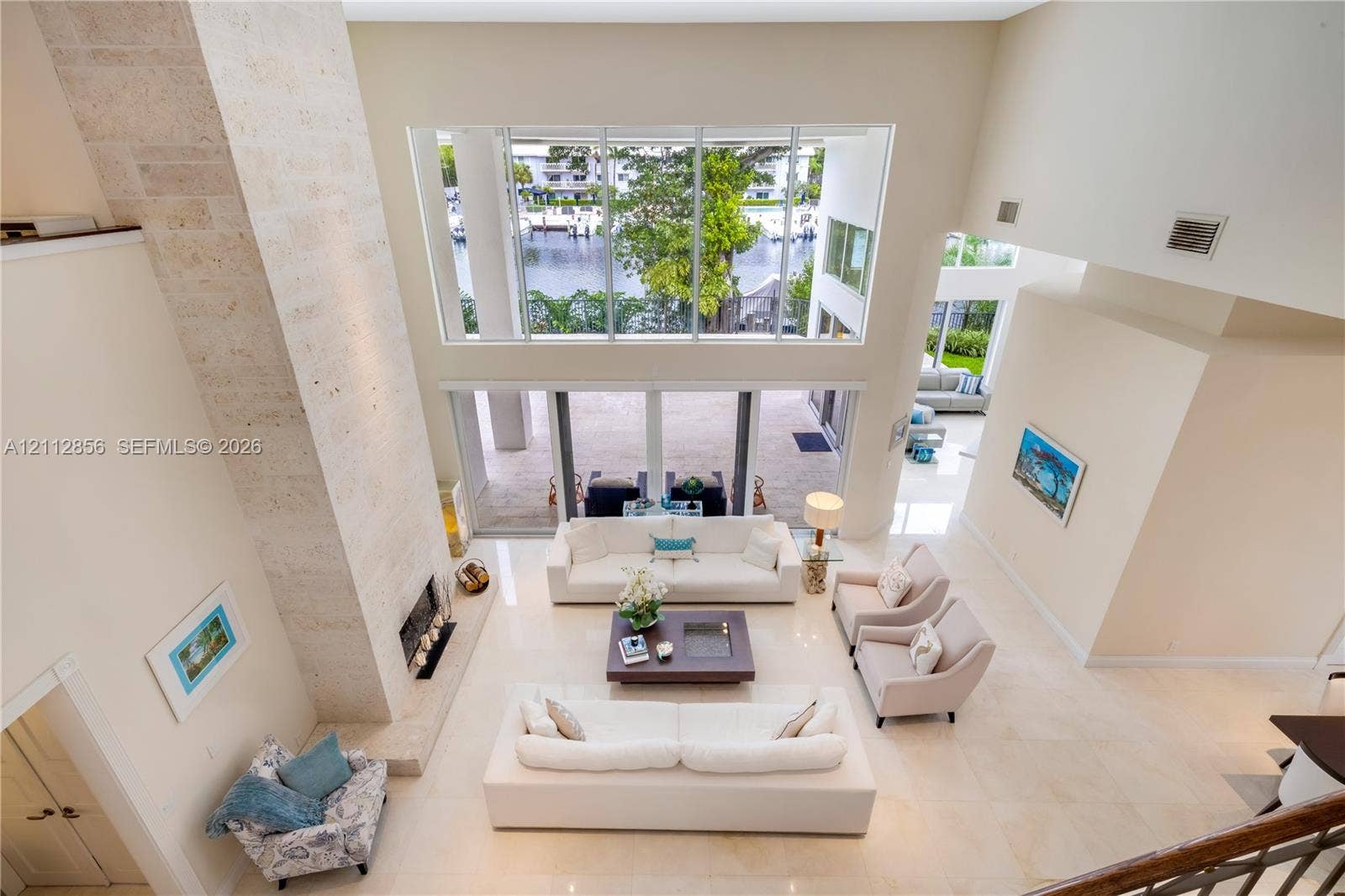 285 Las Brisas Court, Coral Gables, FL 33143 Double-height living area with natural stone fireplace surround, floor-to-ceiling windows, light-toned tile flooring, and direct access to an outdoor patio