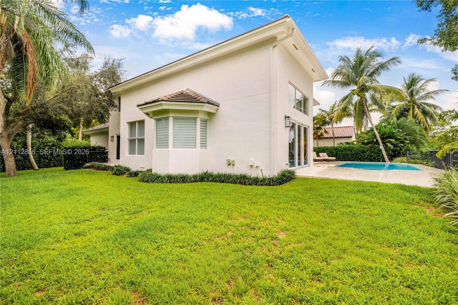 285 Las Brisas Court, Coral Gables, FL 33143 Stucco exterior featuring a bay window, expansive lawn, swimming pool with concrete decking, and floor-to-ceiling glass panel doors