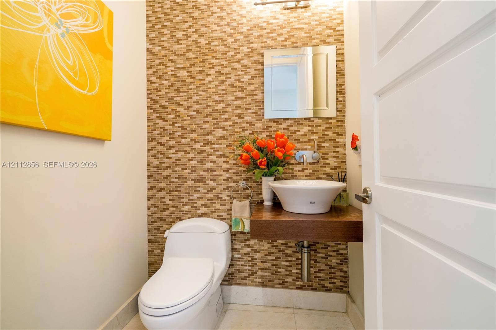 285 Las Brisas Court, Coral Gables, FL 33143 Mosaic tile wall accent, wall-mounted floating wood vanity, white vessel sink with wall-mounted faucet, and square frameless mirror