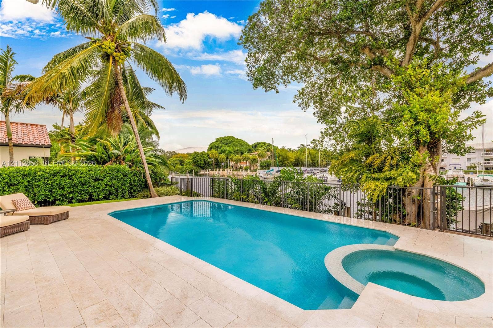 285 Las Brisas Court, Coral Gables, FL 33143 Outdoor pool featuring a built-in spa, paved stone patio, black metal fencing, and mature landscaping