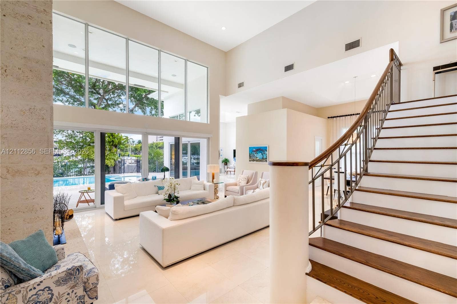285 Las Brisas Court, Coral Gables, FL 33143 Double-height ceilings, floor-to-ceiling glass windows, staircase with wood-finish treads and metal railings, stone-faced interior column, and light-toned tile flooring
