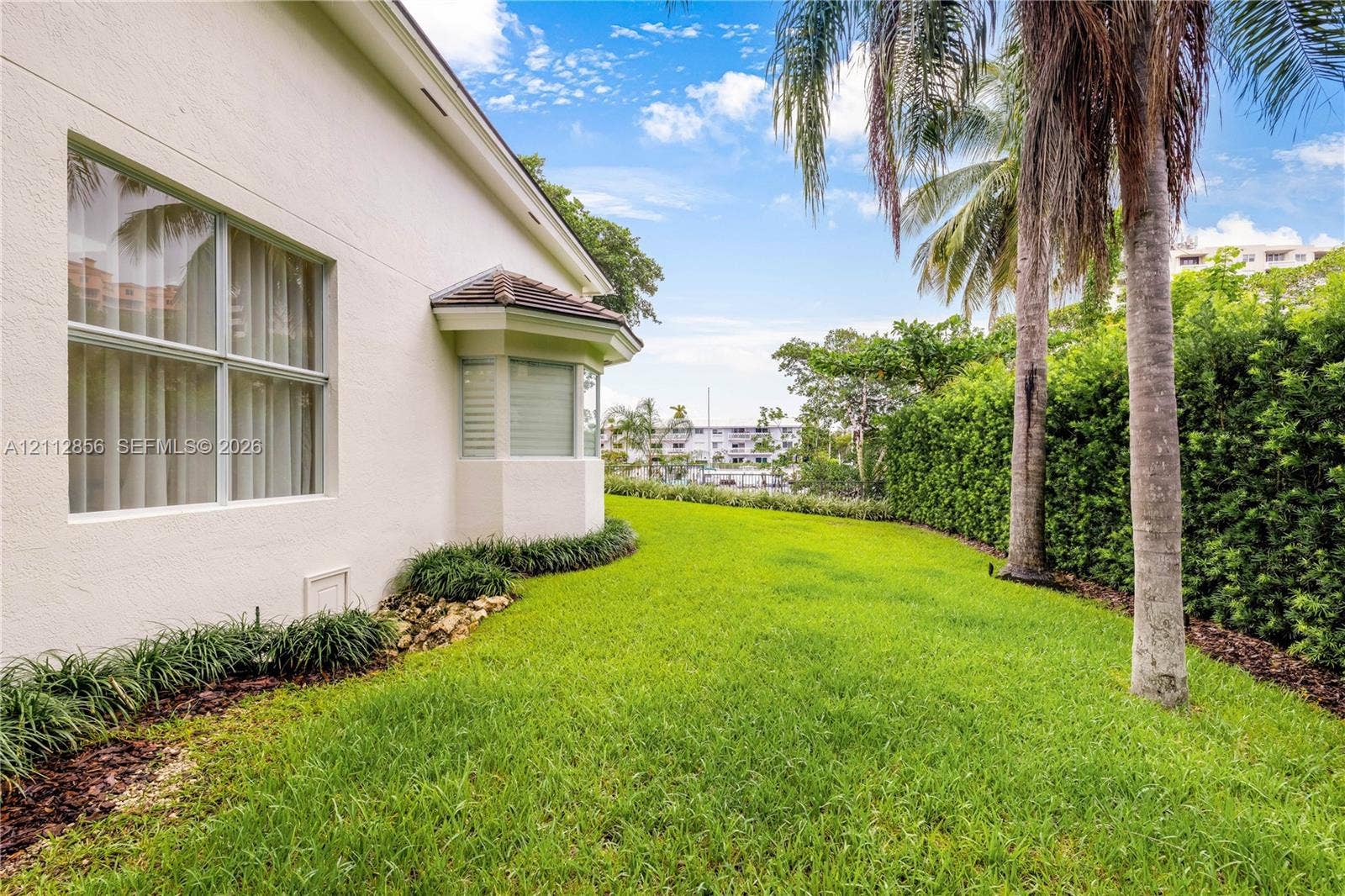 285 Las Brisas Court, Coral Gables, FL 33143 Stucco exterior featuring a bay window, expansive lawn, mature palm trees, and perimeter landscape hedging