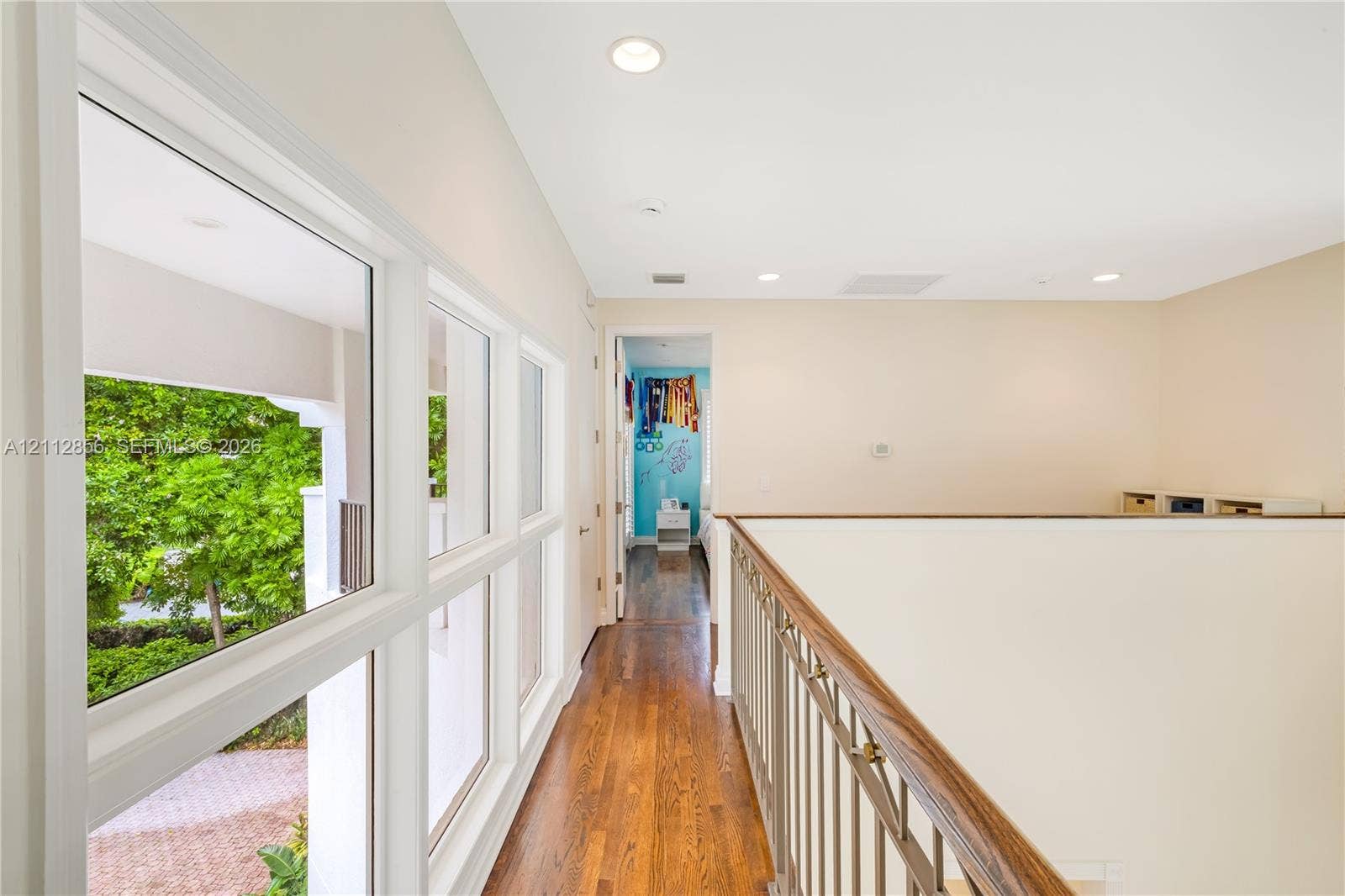 285 Las Brisas Court, Coral Gables, FL 33143 Hallway featuring wood-finish flooring, metal railing with wood-finish handrail, recessed lighting, and large windows