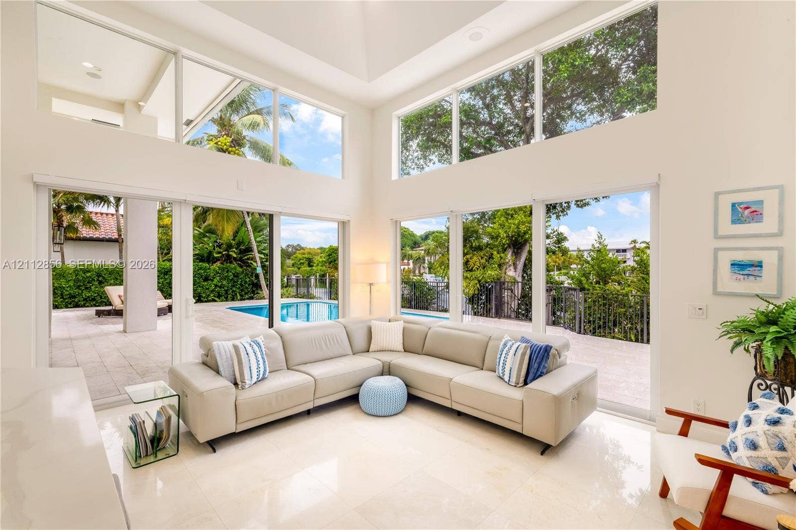 285 Las Brisas Court, Coral Gables, FL 33143 Double-height ceilings, floor-to-ceiling windows, polished stone flooring, and multiple sliding glass doors opening to a paved patio with a swimming pool