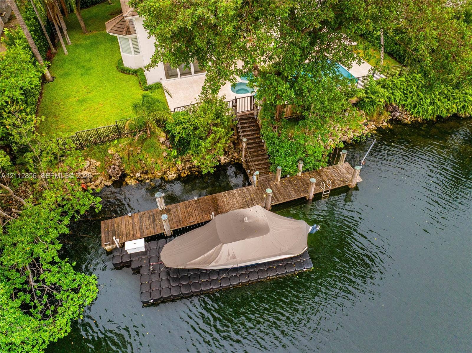285 Las Brisas Court, Coral Gables, FL 33143 Waterfront property featuring a private wooden dock, modular floating boat lift, in-ground pool, integrated spa, and manicured landscaping