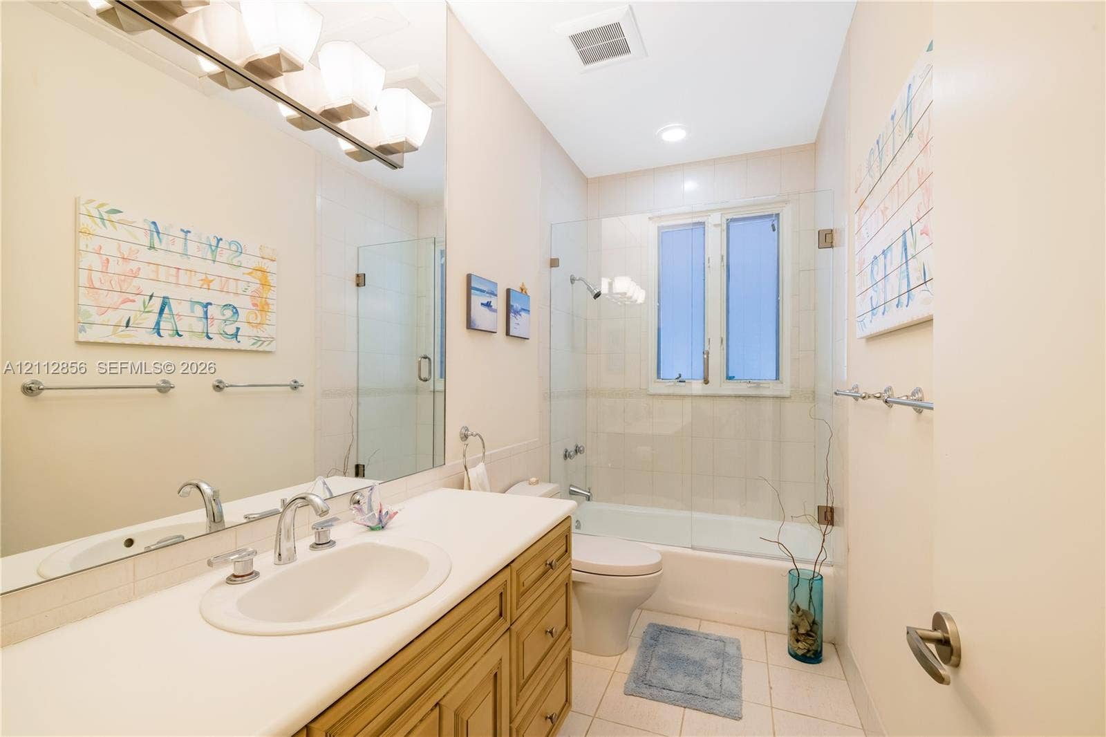 285 Las Brisas Court, Coral Gables, FL 33143 Bathroom featuring wood-finish cabinetry, an integrated sink with a chrome dual-handle faucet, a full-width vanity mirror, and a tub-shower combination enclosed by a frameless glass panel