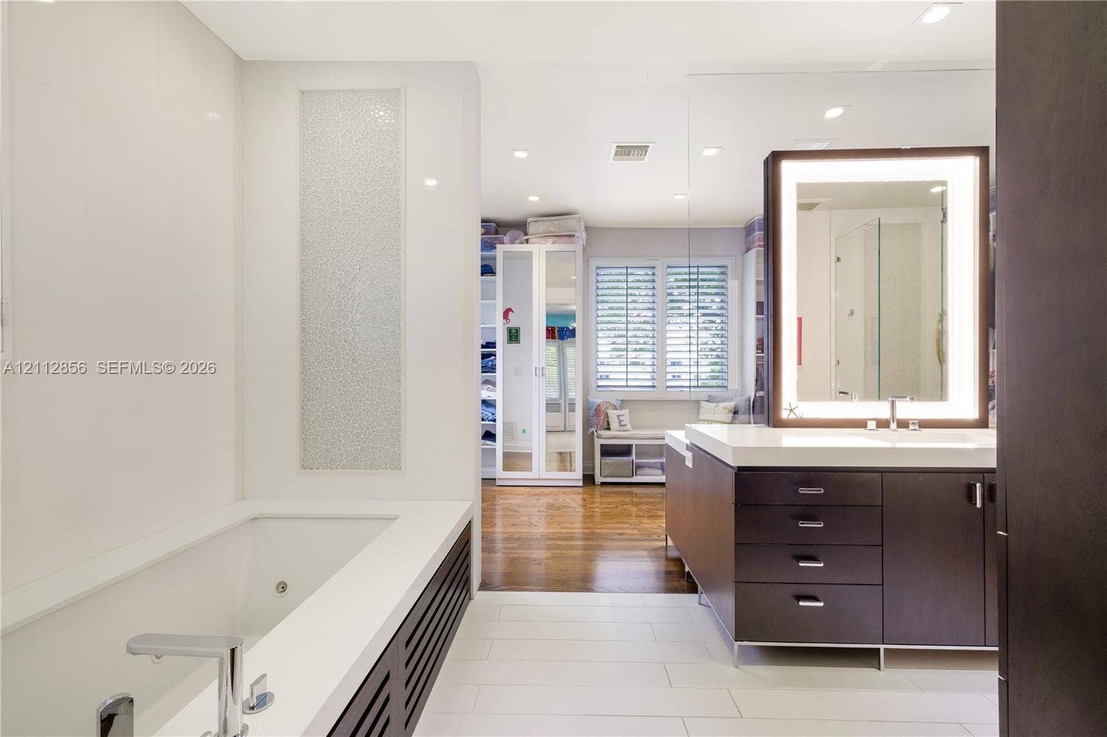 285 Las Brisas Court, Coral Gables, FL 33143 Contemporary bathroom featuring a deep-soaking tub with a tiled surround, custom dark-finish vanity cabinetry with a stone countertop, an integrated LED-lighted mirror, and large-format porcelain floor tile