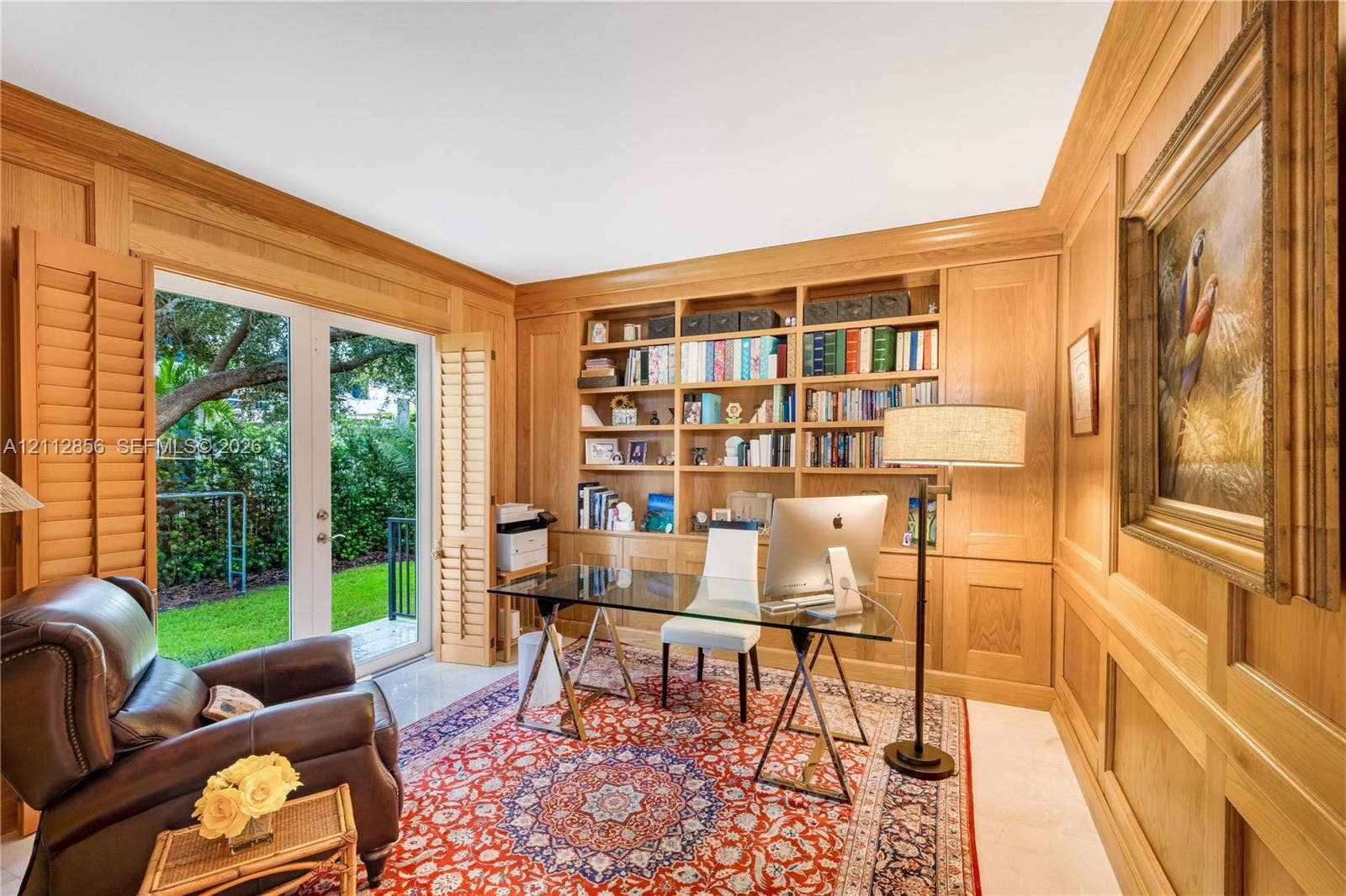 285 Las Brisas Court, Coral Gables, FL 33143 Wood-paneled room featuring custom floor-to-ceiling built-in bookshelves, light-finish tile flooring, and glass French doors with integrated louvered shutters