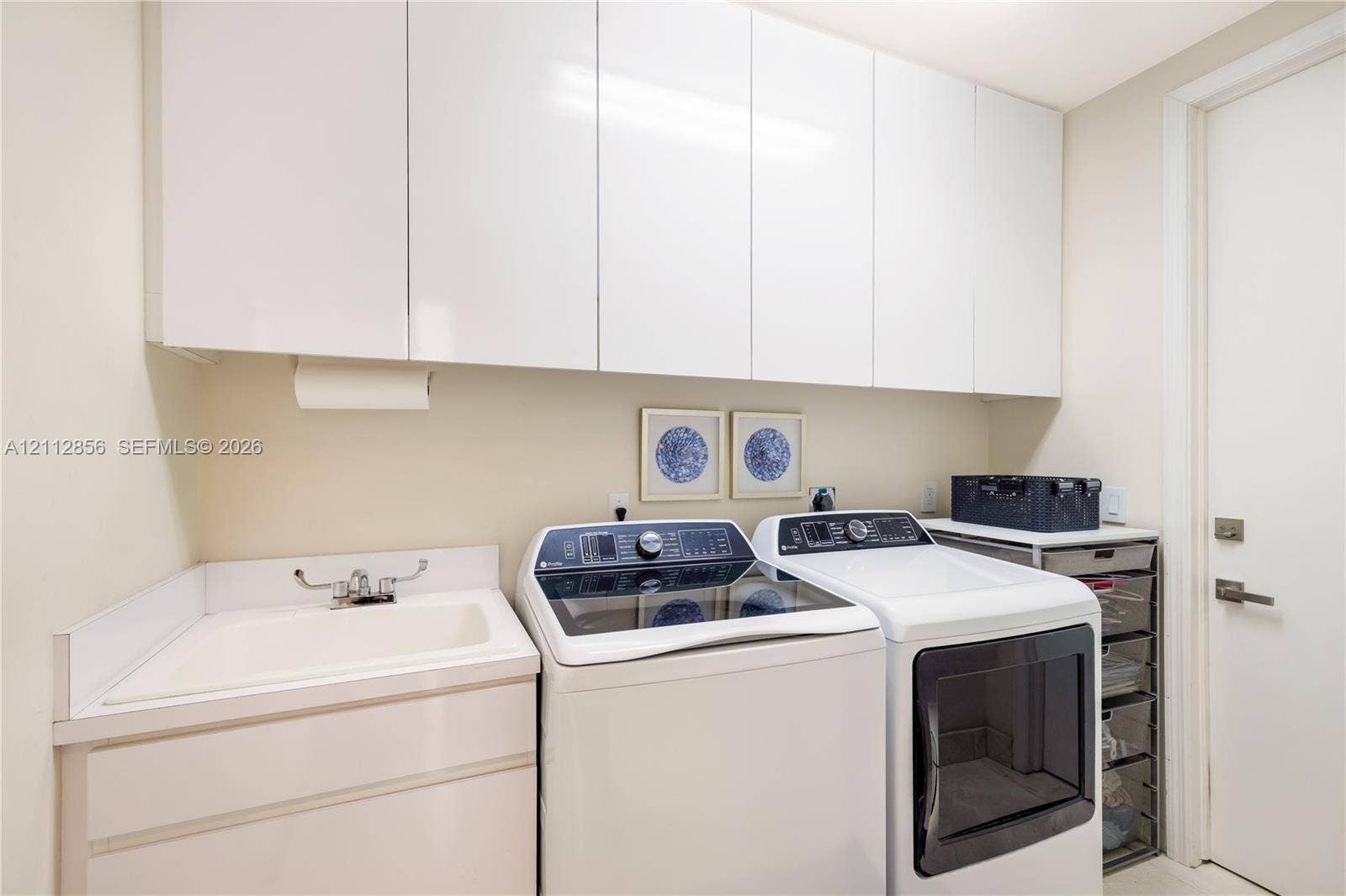 285 Las Brisas Court, Coral Gables, FL 33143 Laundry area featuring sleek white cabinetry, a built-in utility sink with a chrome faucet, and ample overhead storage