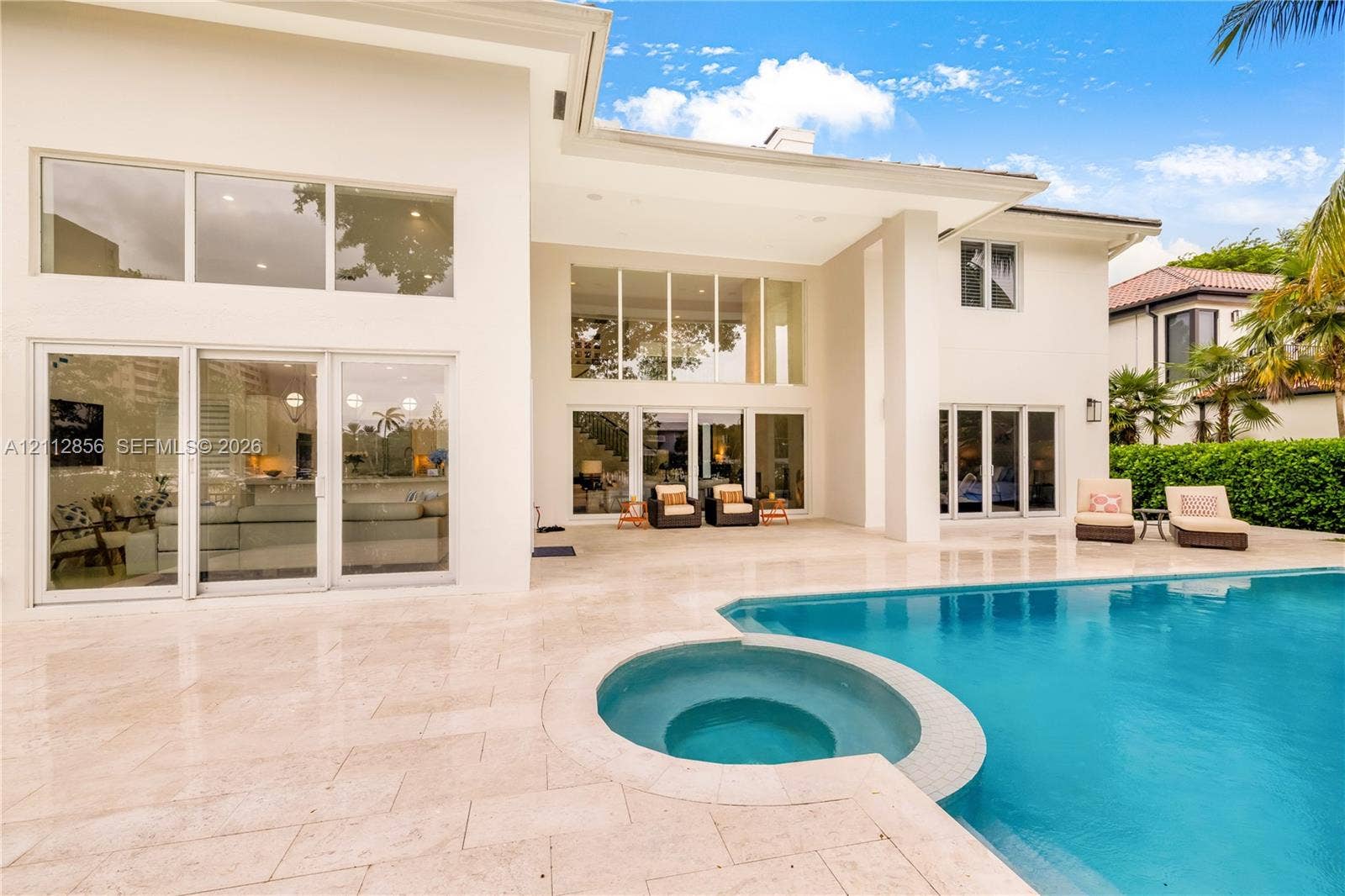 285 Las Brisas Court, Coral Gables, FL 33143 Exterior elevation featuring a stucco facade, expansive glass walls with multi-panel sliding doors, a stone-paved patio, and a swimming pool with a built-in spa