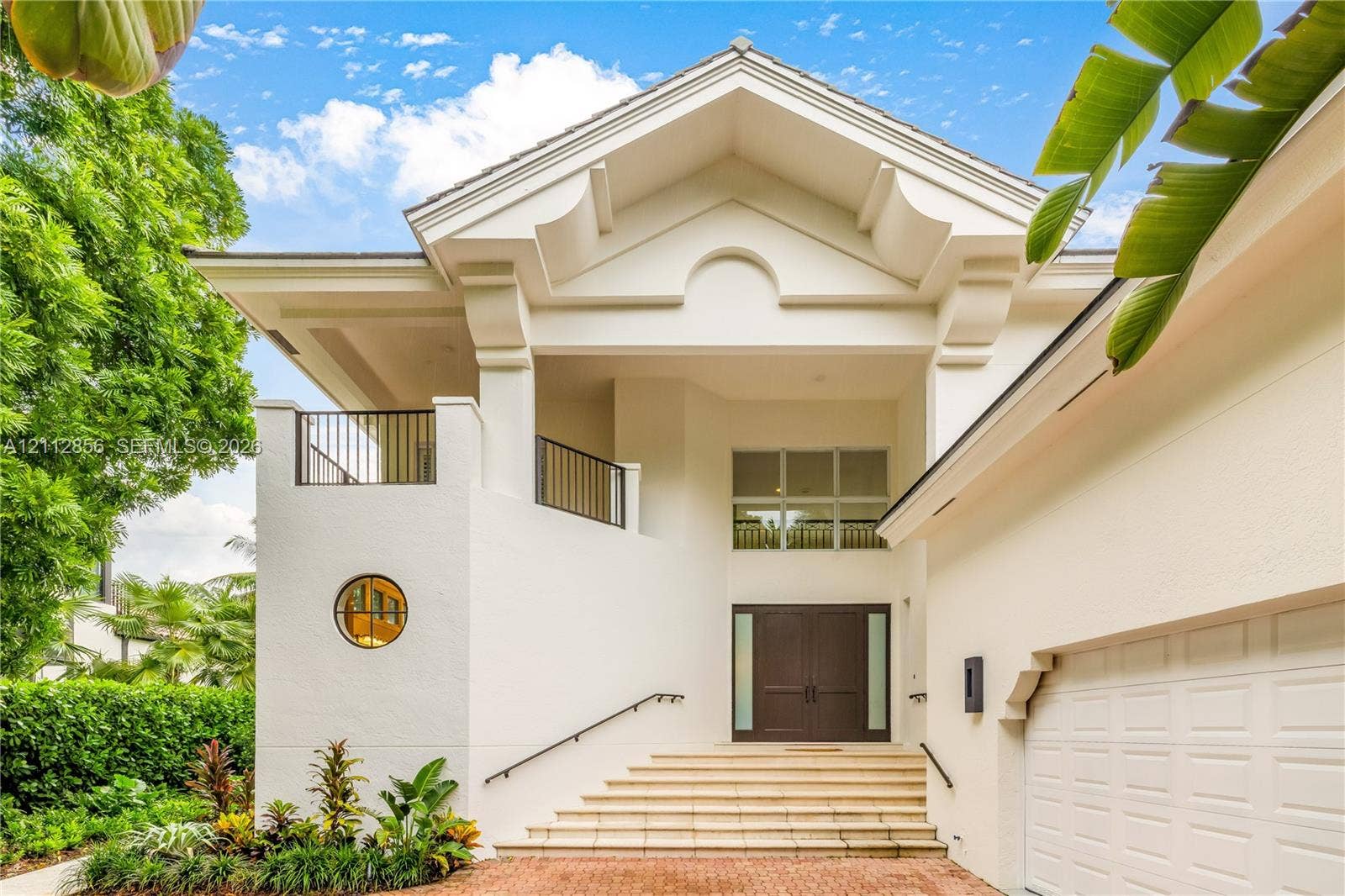285 Las Brisas Court, Coral Gables, FL 33143 Architectural exterior featuring a vaulted gabled roofline, decorative corbels, a private second-story balcony with metal railings, a circular accent window, and double-entry doors