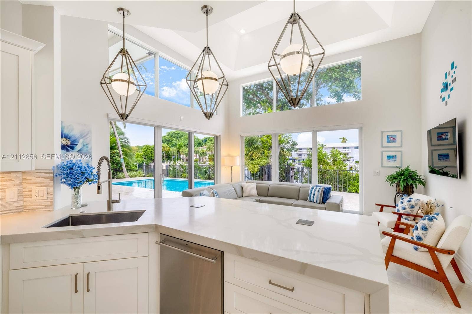 285 Las Brisas Court, Coral Gables, FL 33143 Kitchen island featuring a quartz countertop and stainless steel under-mount sink, high ceilings, geometric metal pendant lighting, and floor-to-ceiling glass panel doors