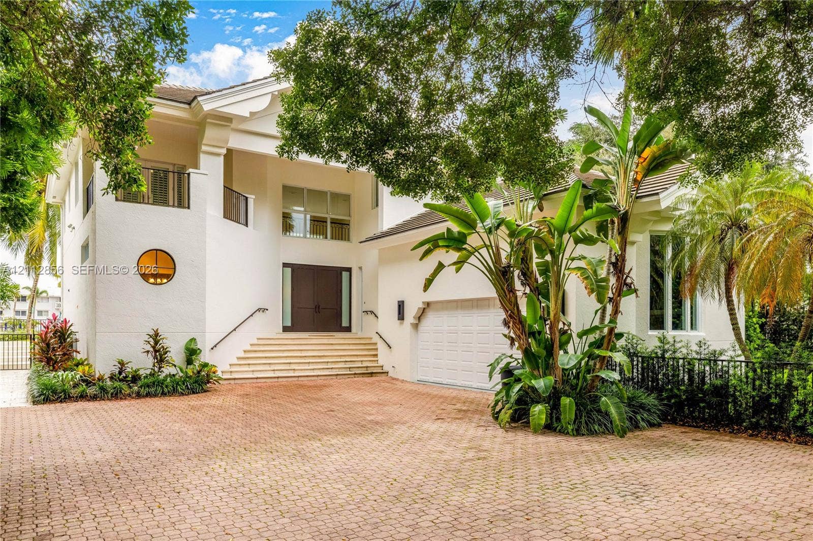 285 Las Brisas Court, Coral Gables, FL 33143 Two-story exterior featuring a paver driveway, double front doors, an elevated entryway with stone steps, a circular accent window, and a built-in garage